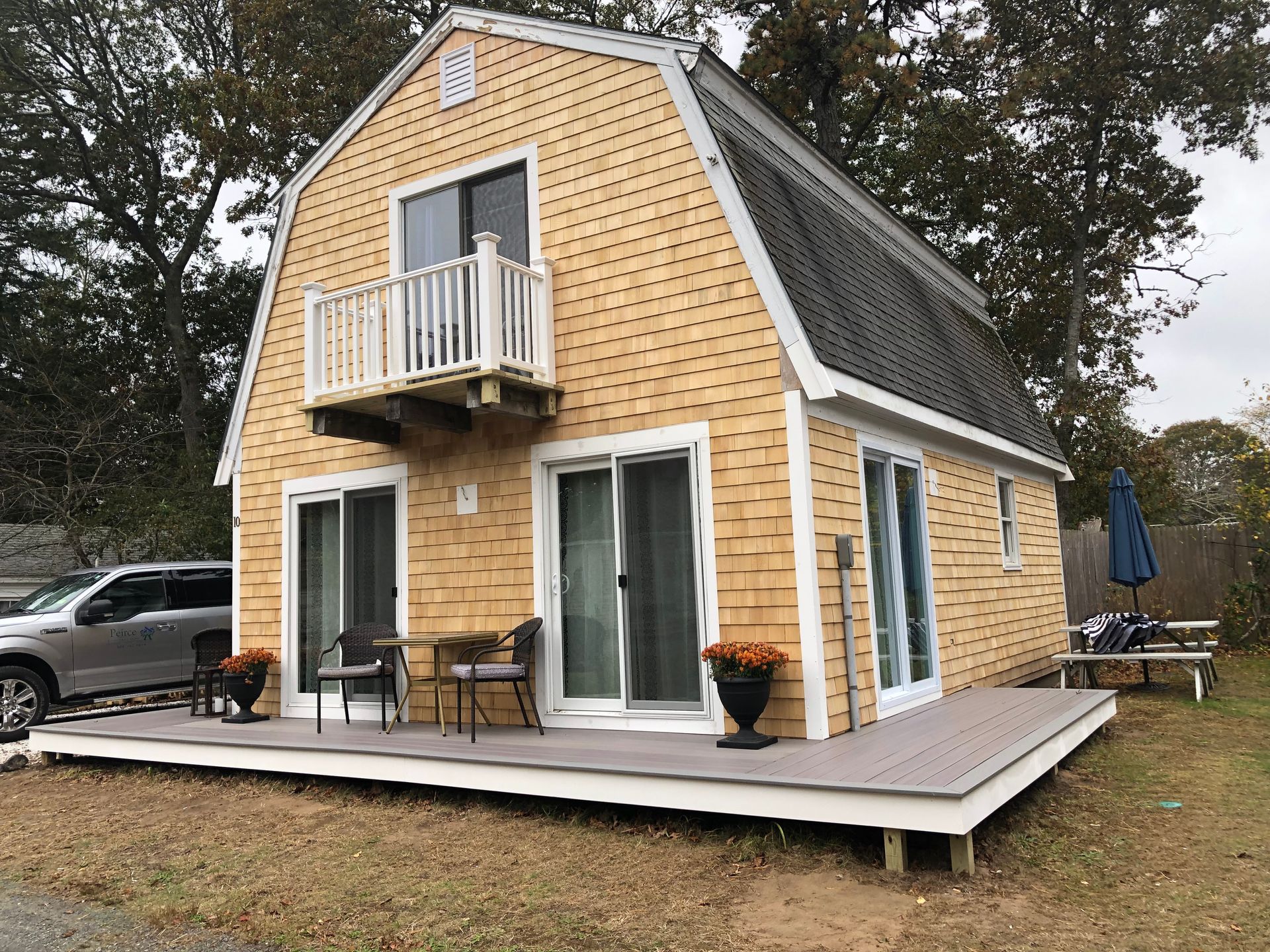 Yellow-sided barn-style cottage with white trim, deck, and sliding glass doors.  A car is parked to the left.