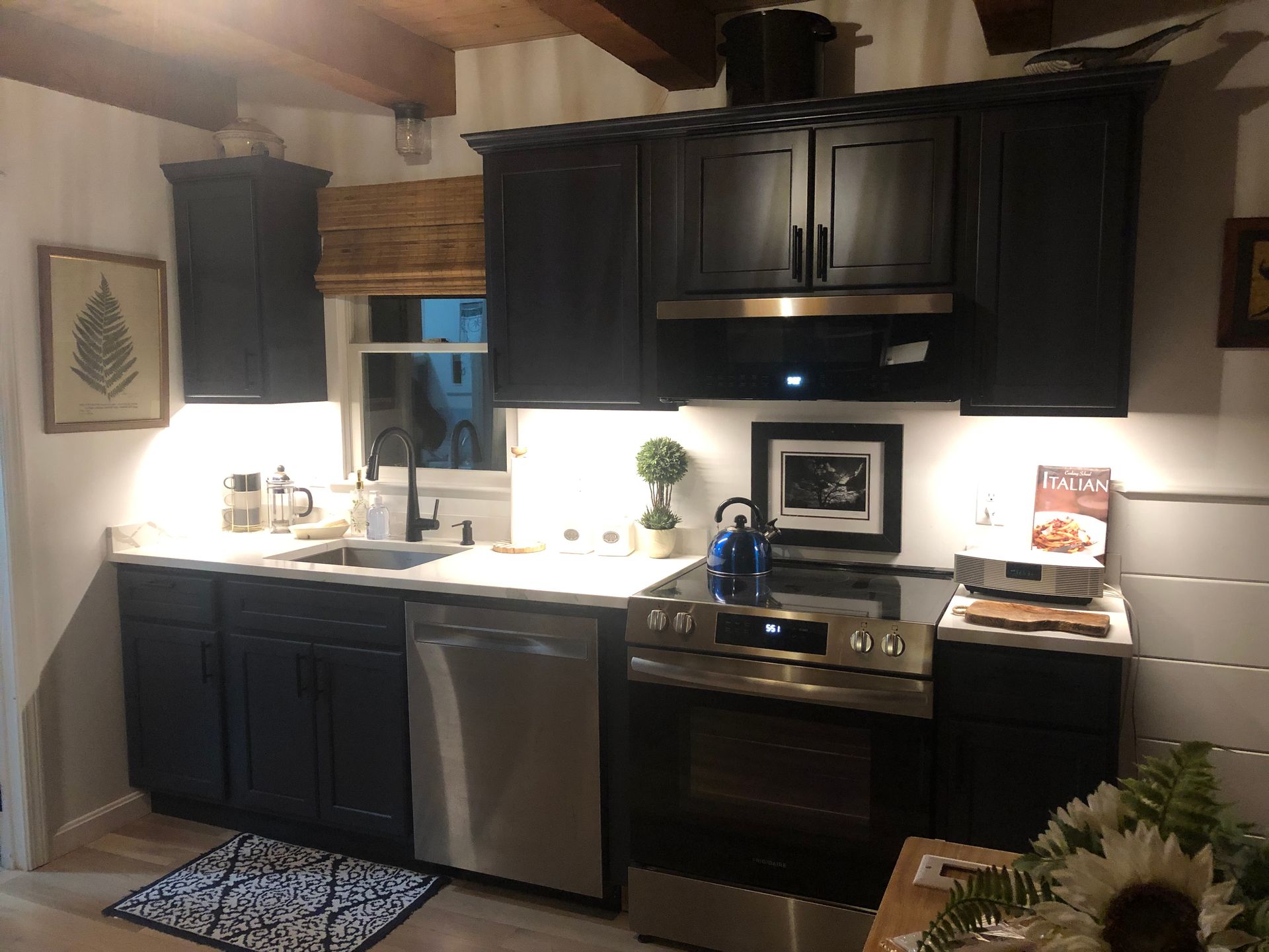 Dark-painted kitchen cabinets with stainless steel appliances and under-cabinet lighting.