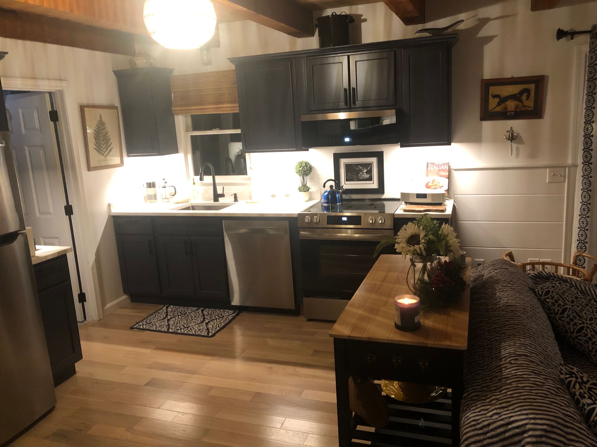 Cozy kitchen with dark cabinets, white countertops, and wooden table. A lit candle sits on the table.