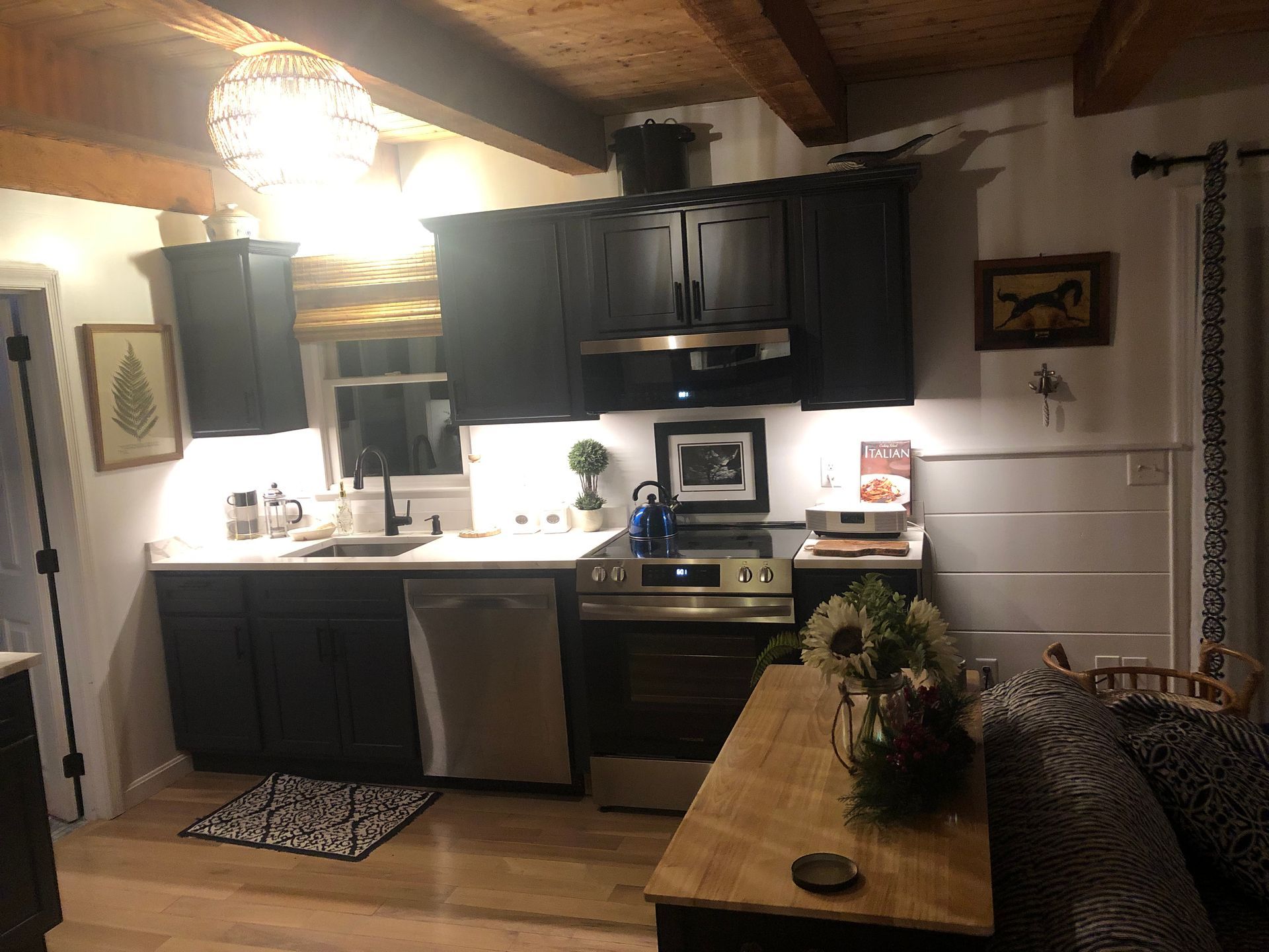Cozy kitchen with dark cabinets, white countertops, and wooden ceiling. Features a stove, sink, and small table.
