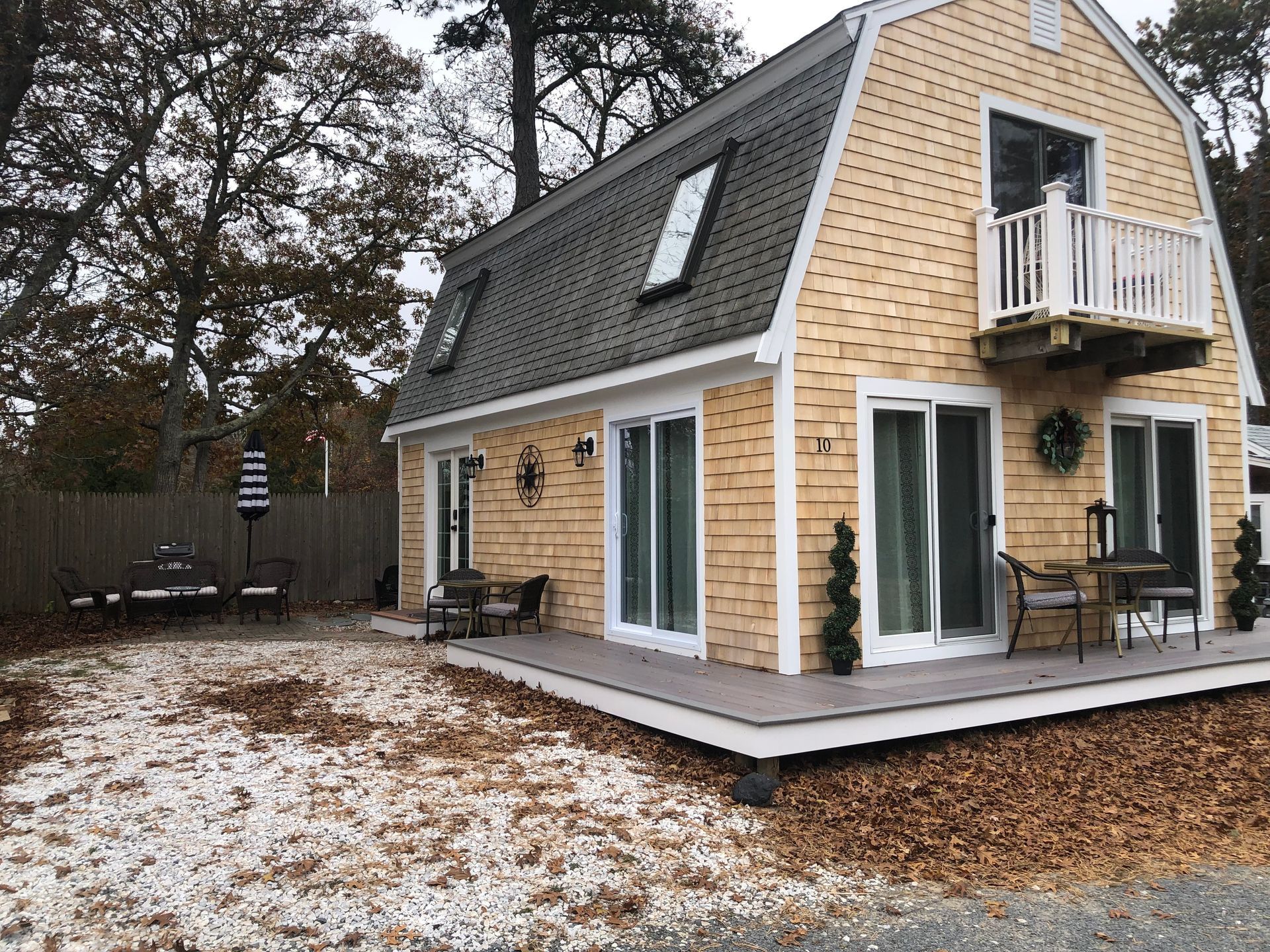 Light-yellow shingled house with dark roof and small balcony. Sliding glass doors open to a deck.