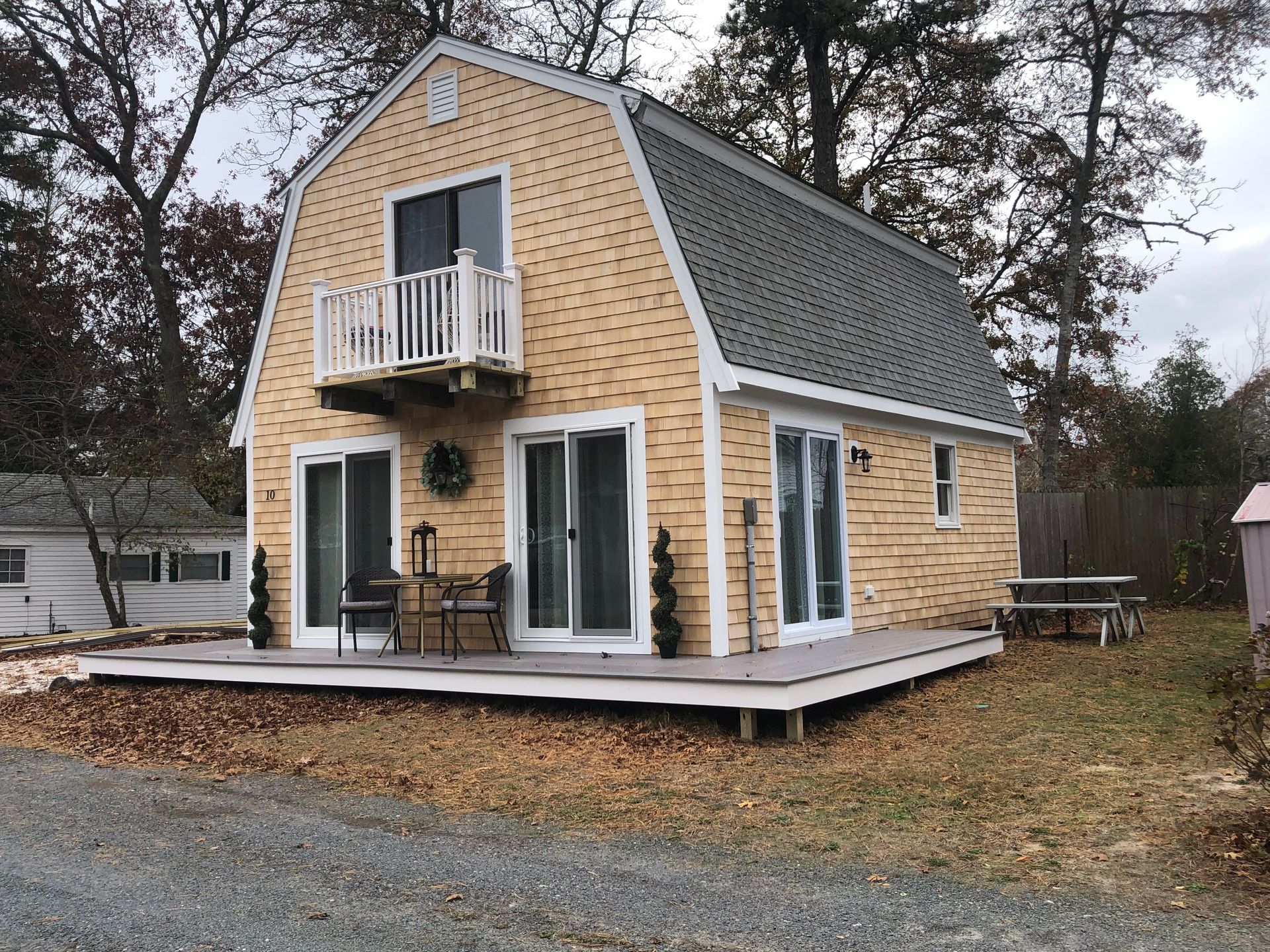 Small, yellow Dutch-style house with a deck and sliding glass doors.  A small balcony is above the front door.