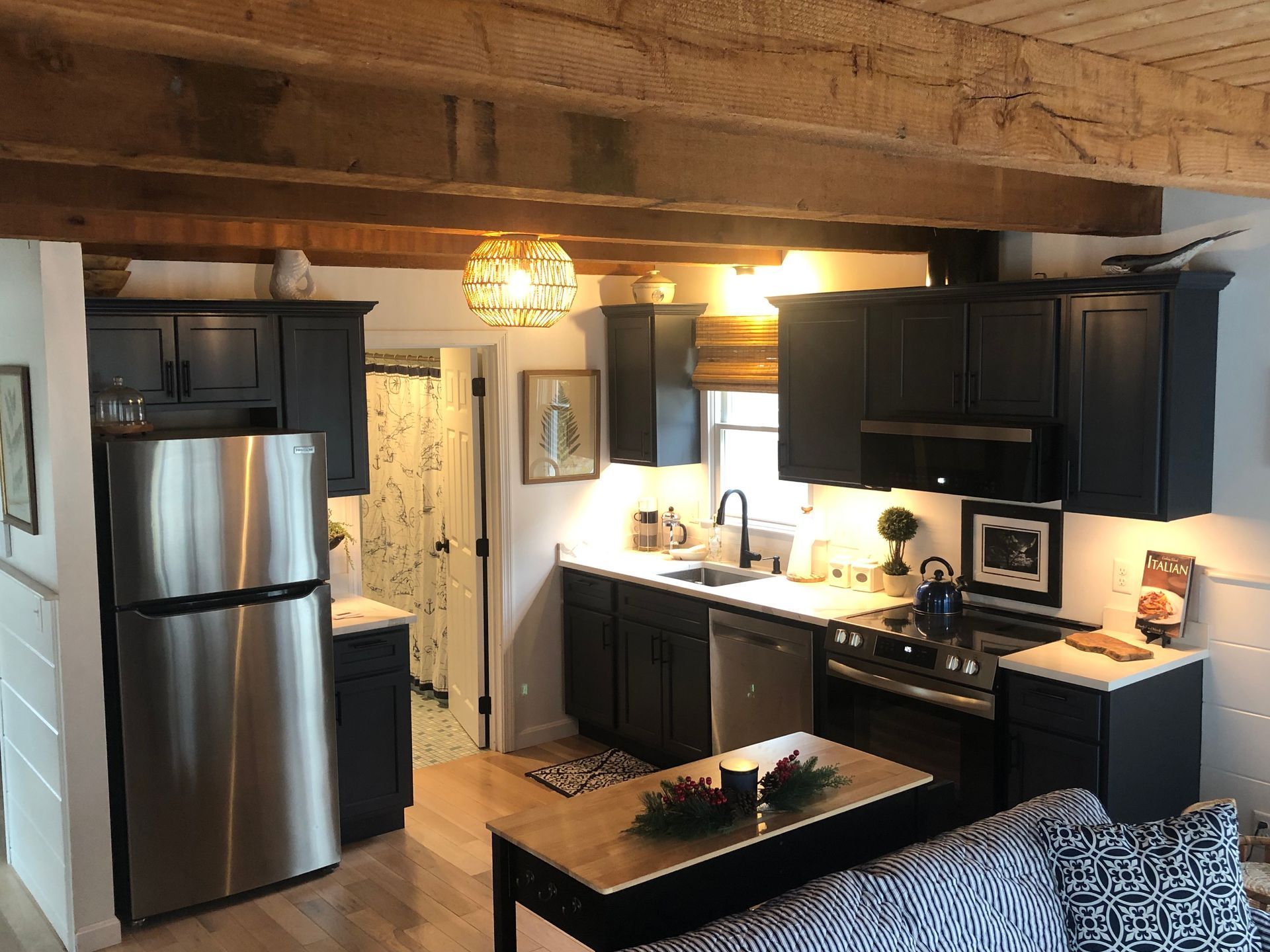 Small kitchen with black cabinets, stainless steel appliances, and wooden ceiling beams.