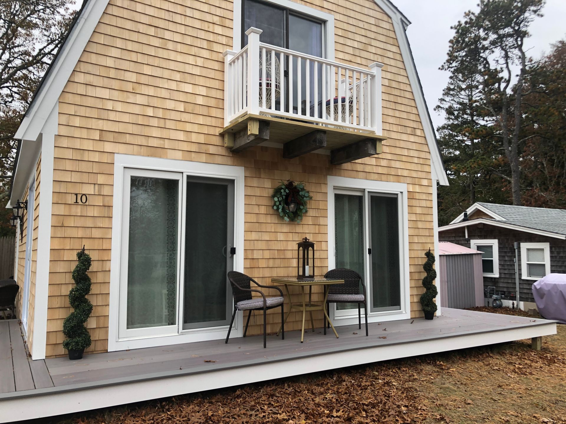 Cottage with shingle siding, a small balcony, and a deck with outdoor seating.
