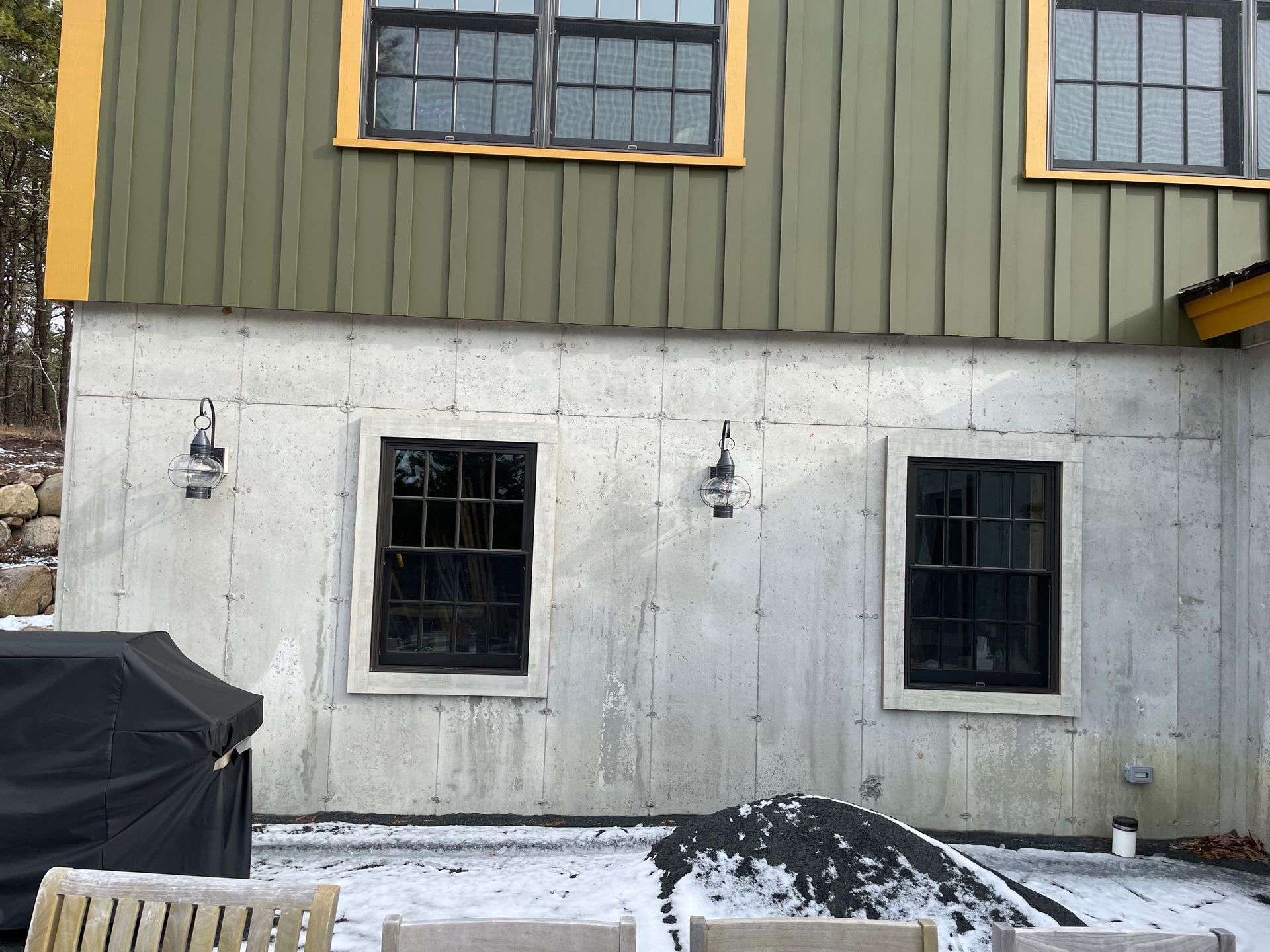 Gray building exterior with dark-framed windows, green siding above, and snow on the ground.