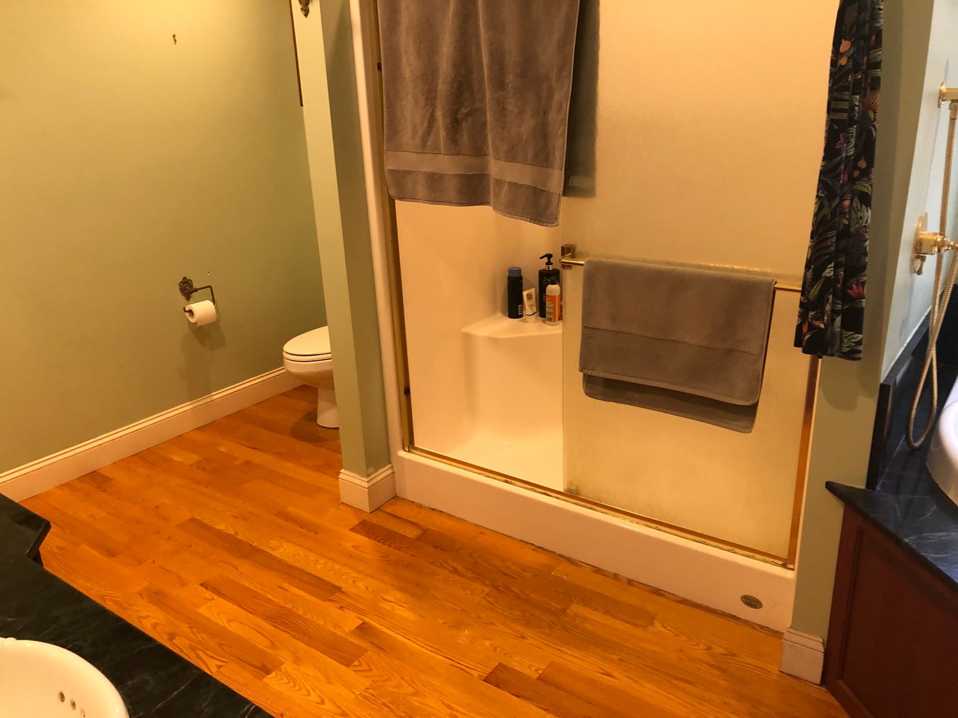 Bathroom with wood floor, green walls, shower stall, and toilet. A towel hangs near the shower.