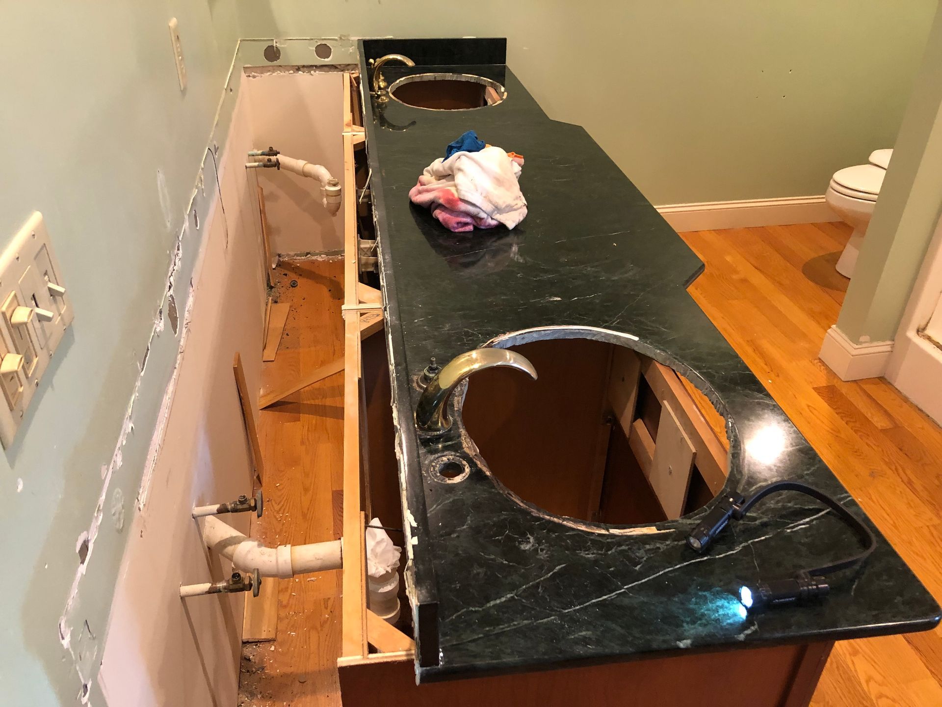 Bathroom vanity with two sink cutouts, plumbing exposed in the wall, and a green countertop.