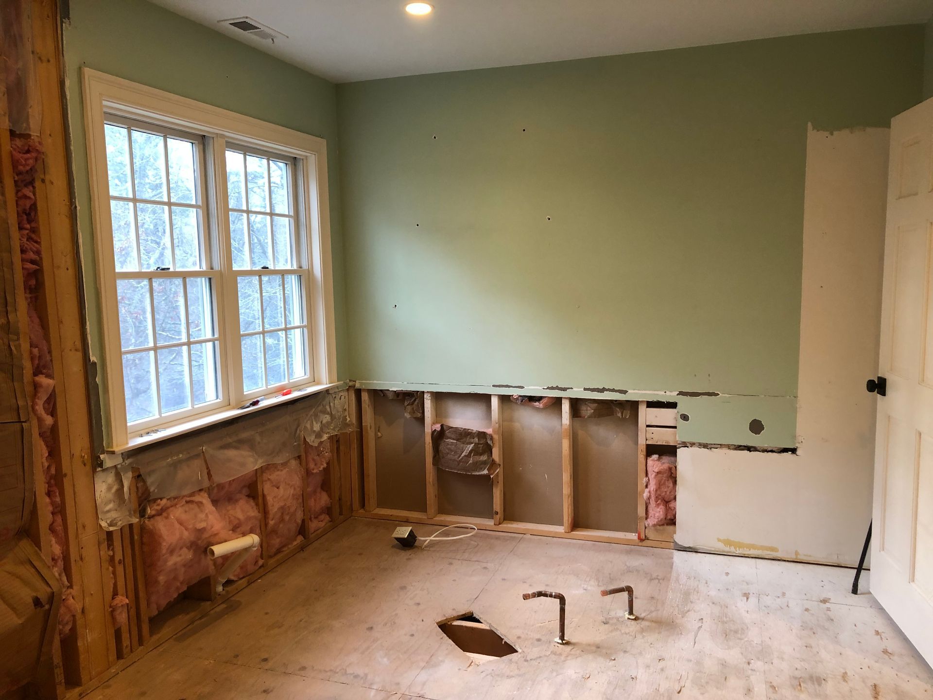 Bathroom renovation in progress; exposed wall studs, pink insulation, window, light green wall, and door.