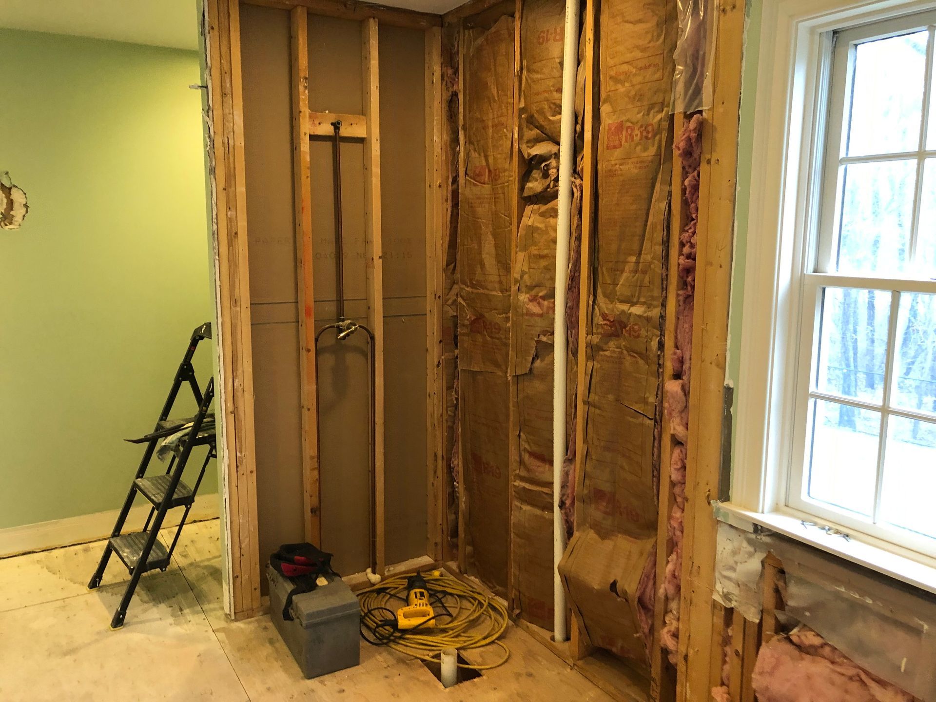 Bathroom renovation in progress, framing and insulation exposed, with window and ladder visible.