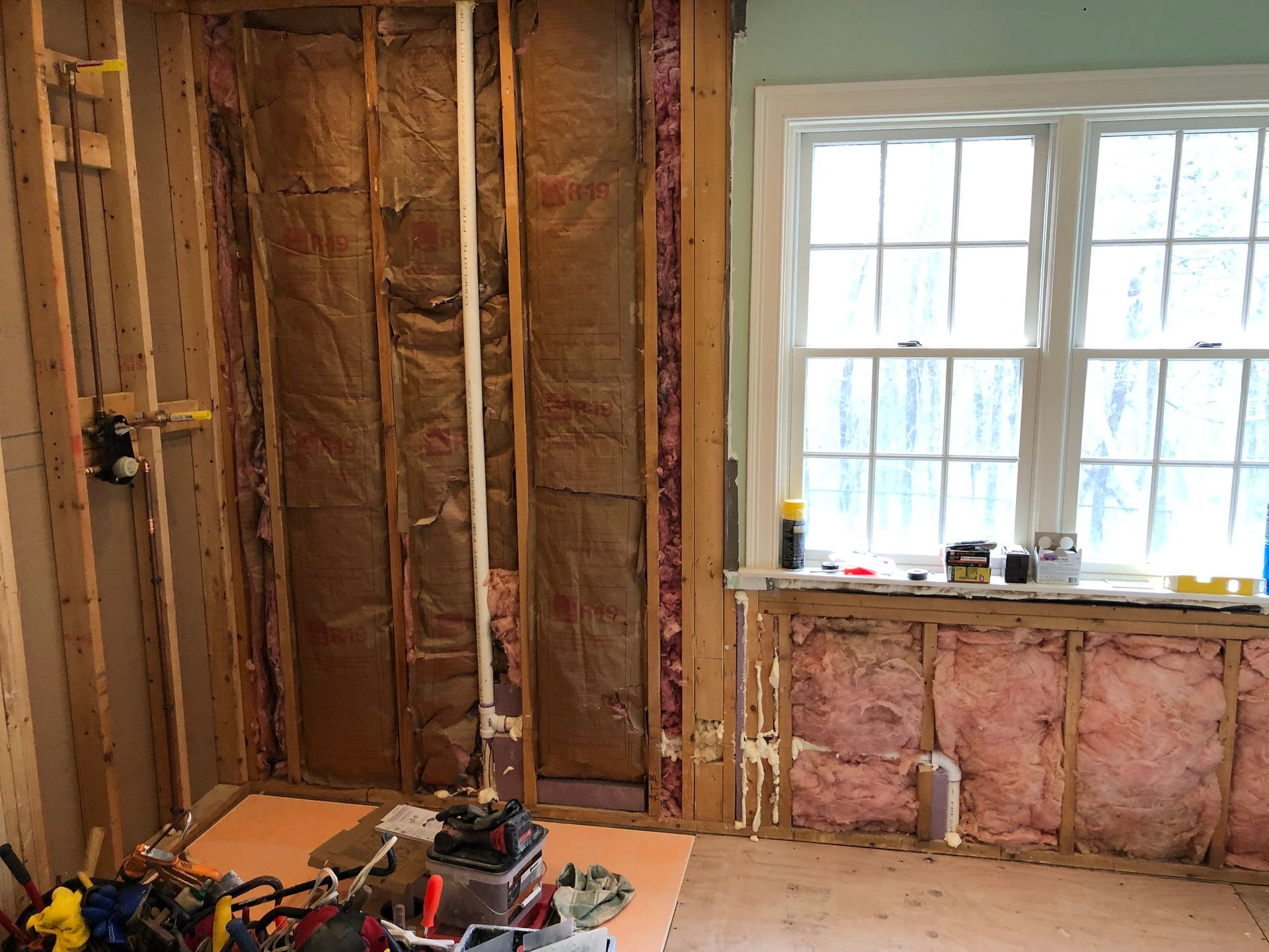Bathroom remodel in progress; exposed studs, insulation, window, tools visible.