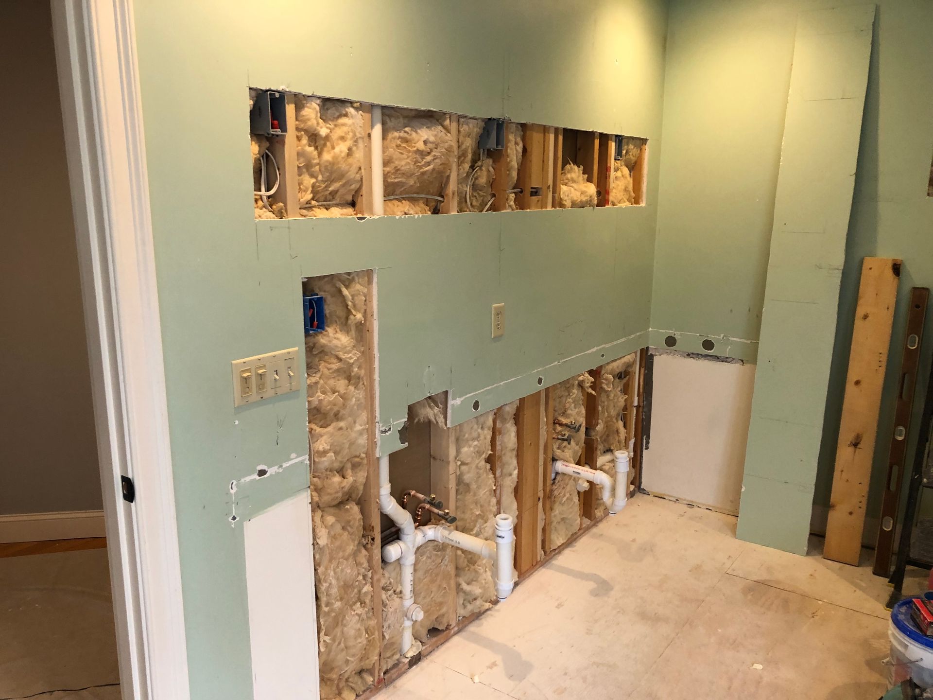 Interior view of a room under construction; drywall partially installed, exposing plumbing and insulation.