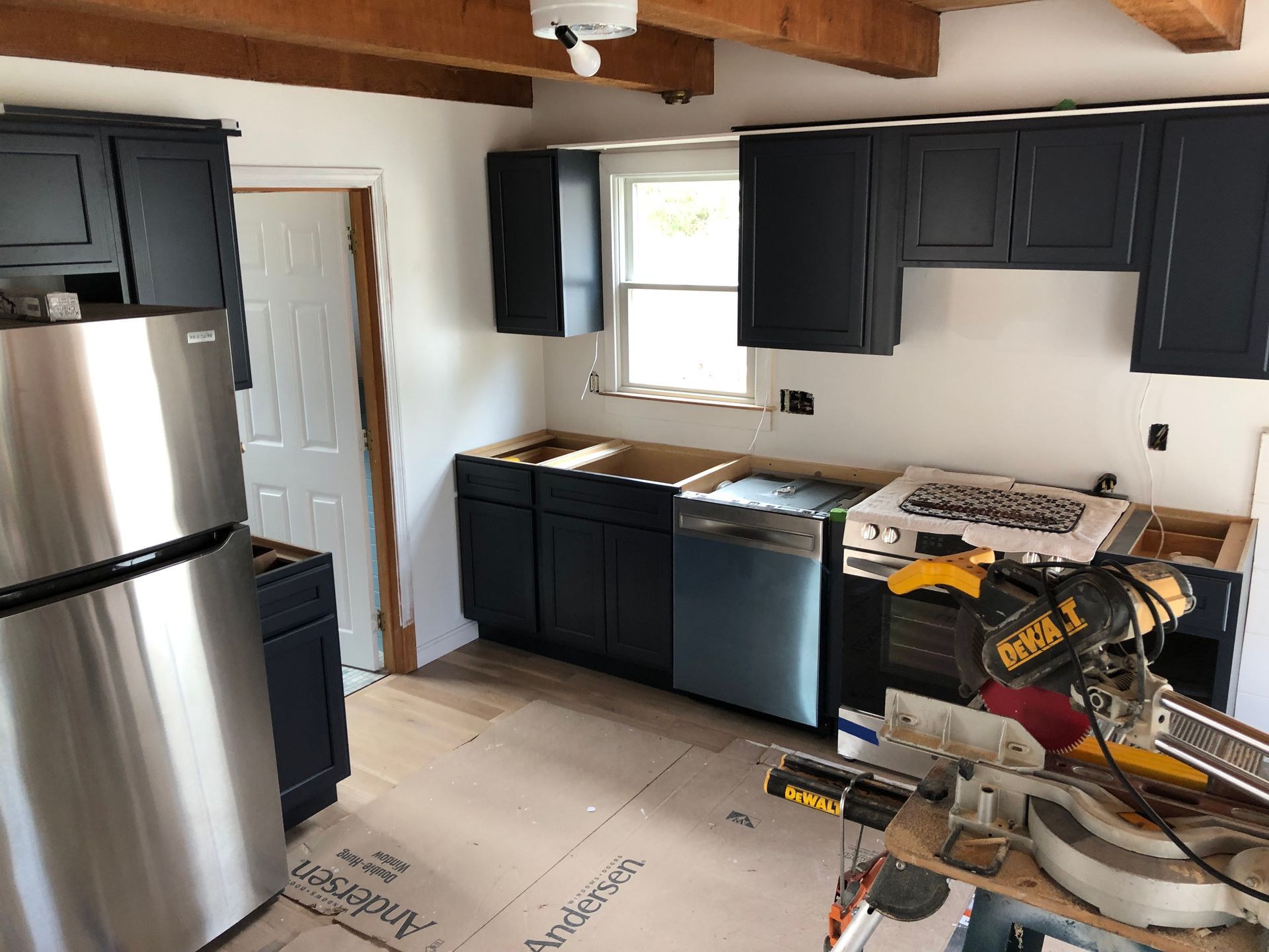 Kitchen under construction with dark blue cabinets, stainless steel appliances, and tools.