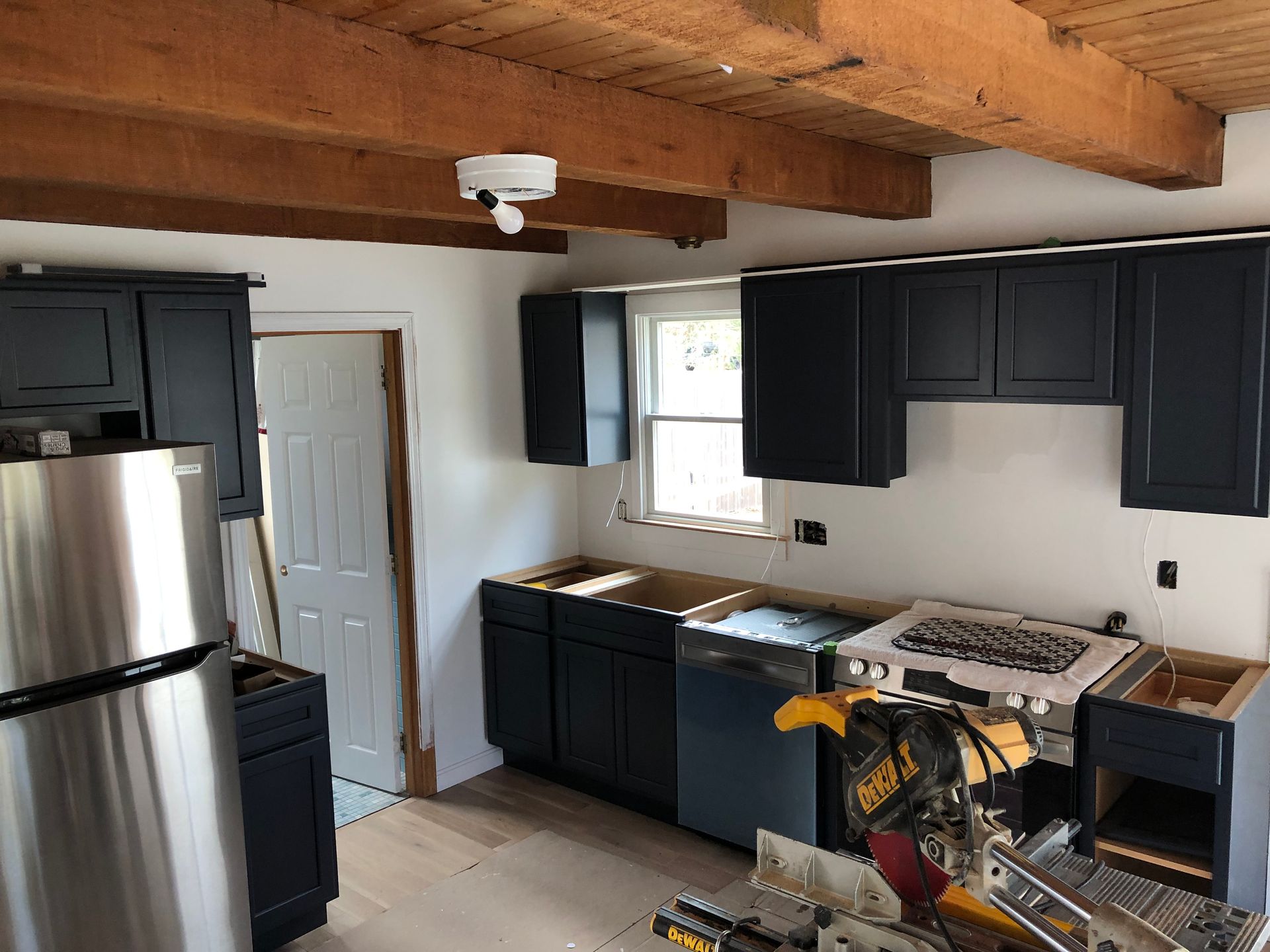Kitchen with dark blue cabinets and wooden beams. A refrigerator and miter saw are visible.