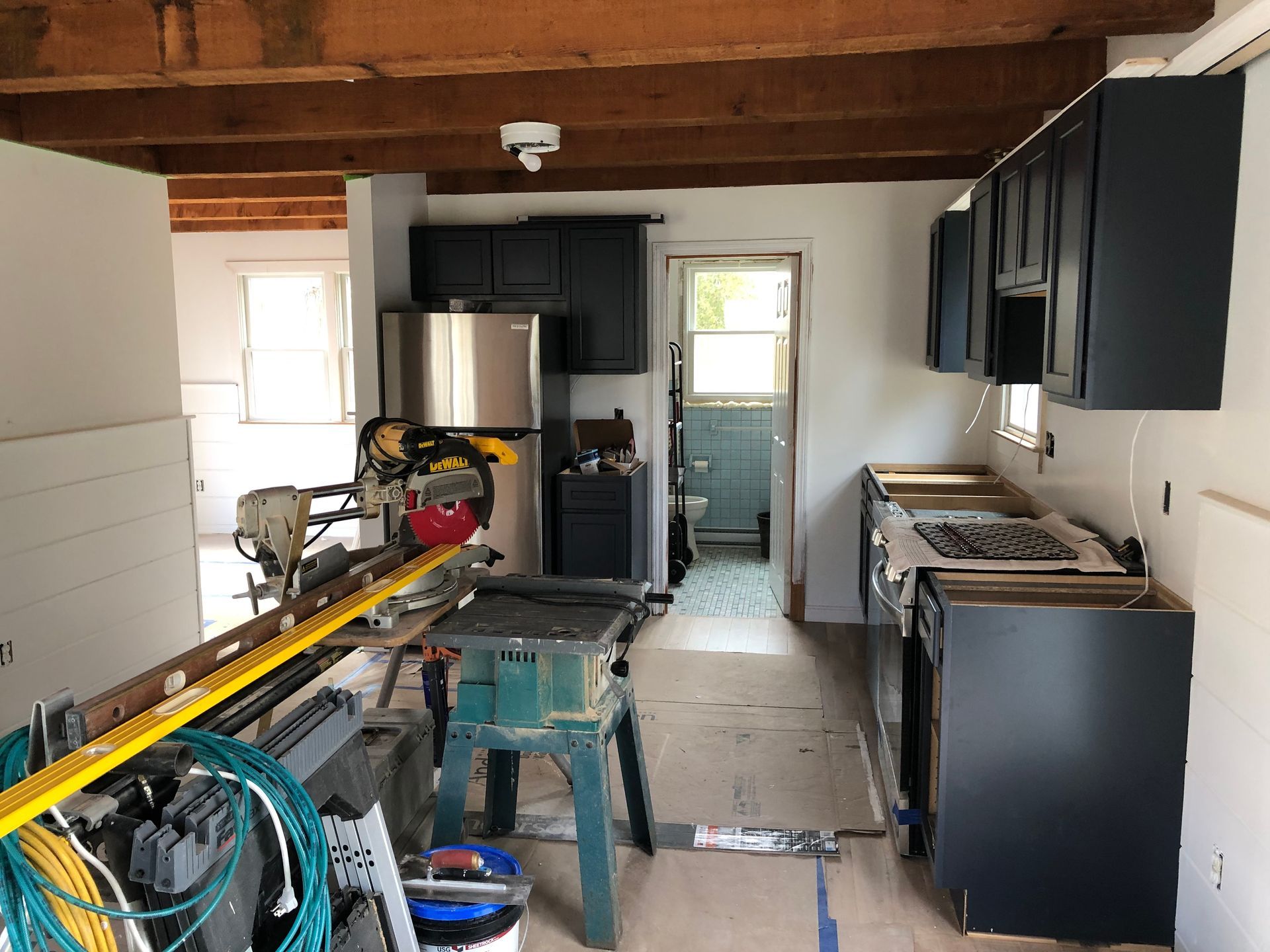 Kitchen under construction with dark blue cabinets, unfinished countertops, and tools scattered about.