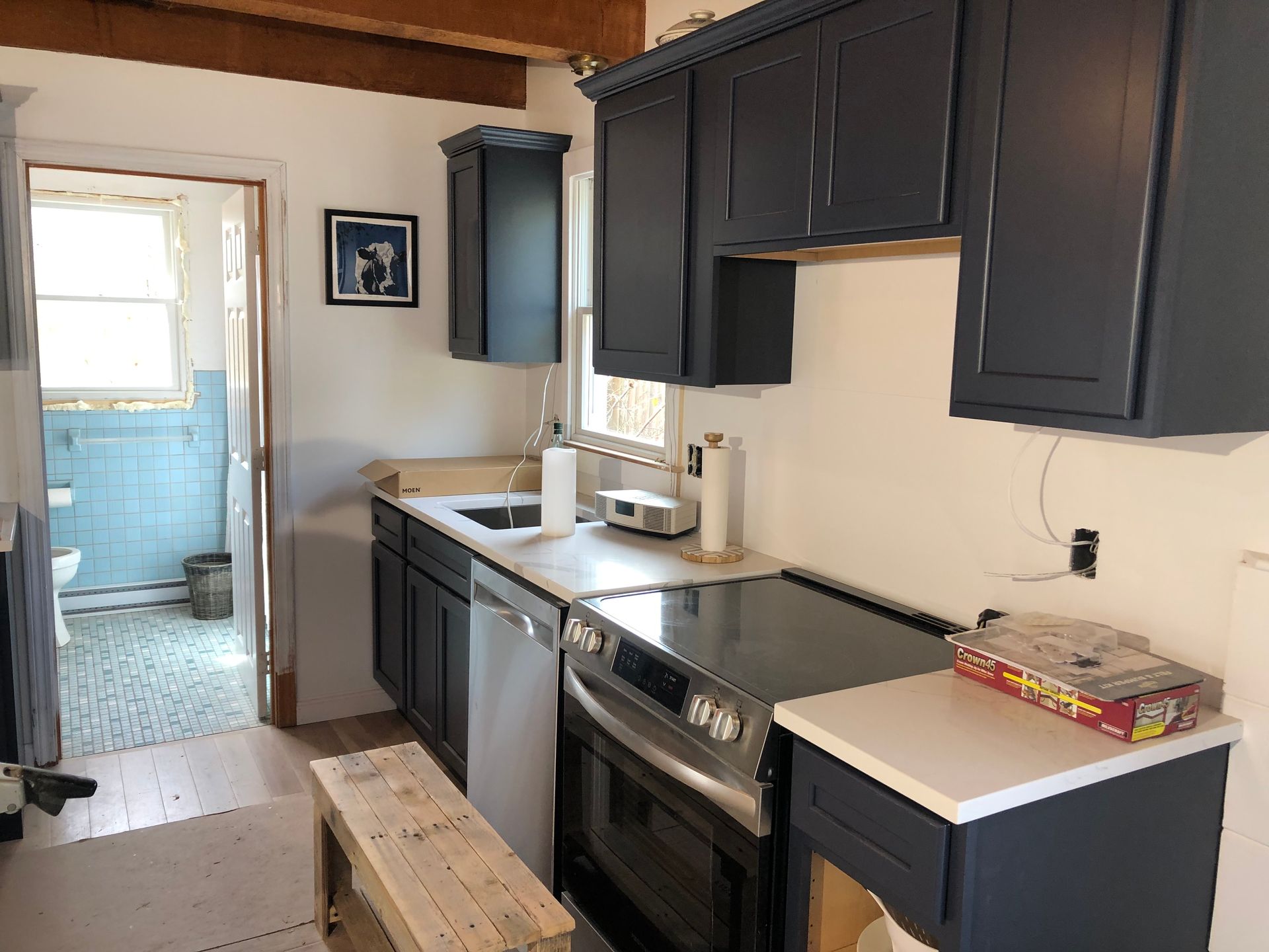 Kitchen with dark blue cabinets, white countertops, and open doorway to a blue-tiled bathroom.