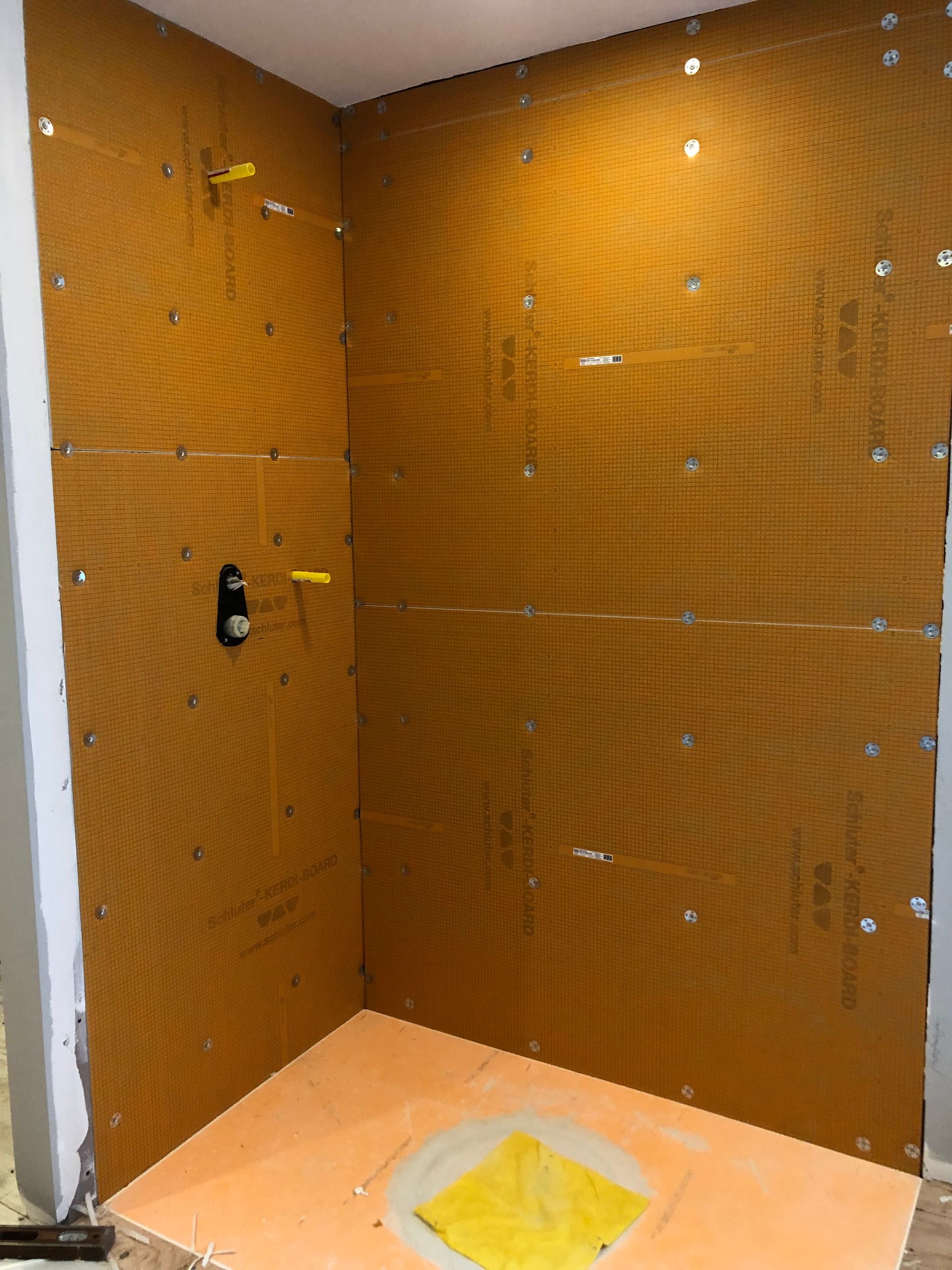 Shower stall under construction, orange waterproof backer board installed on walls and floor.