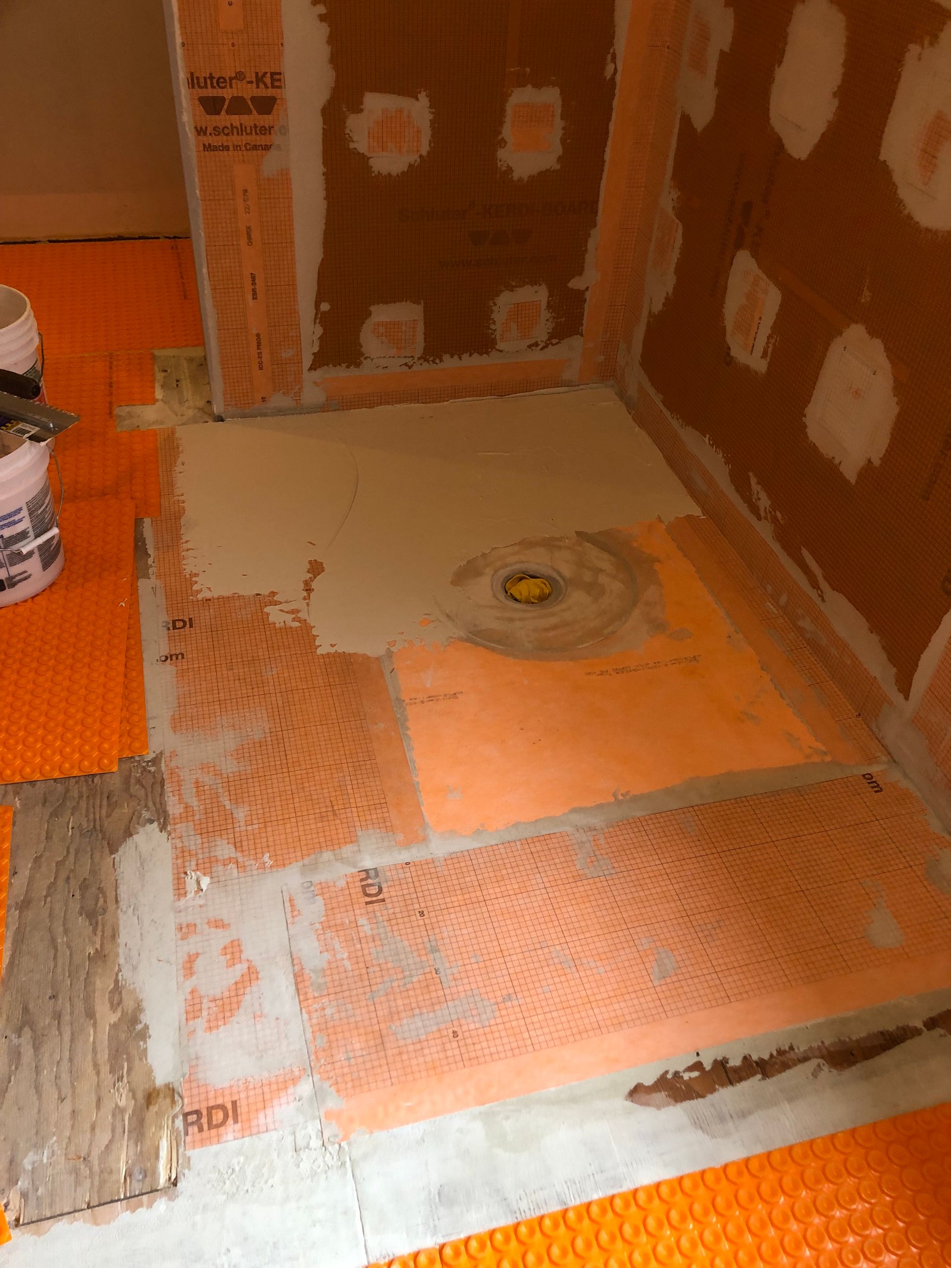 Shower pan under construction; orange waterproof membrane, mortar, and drain visible.