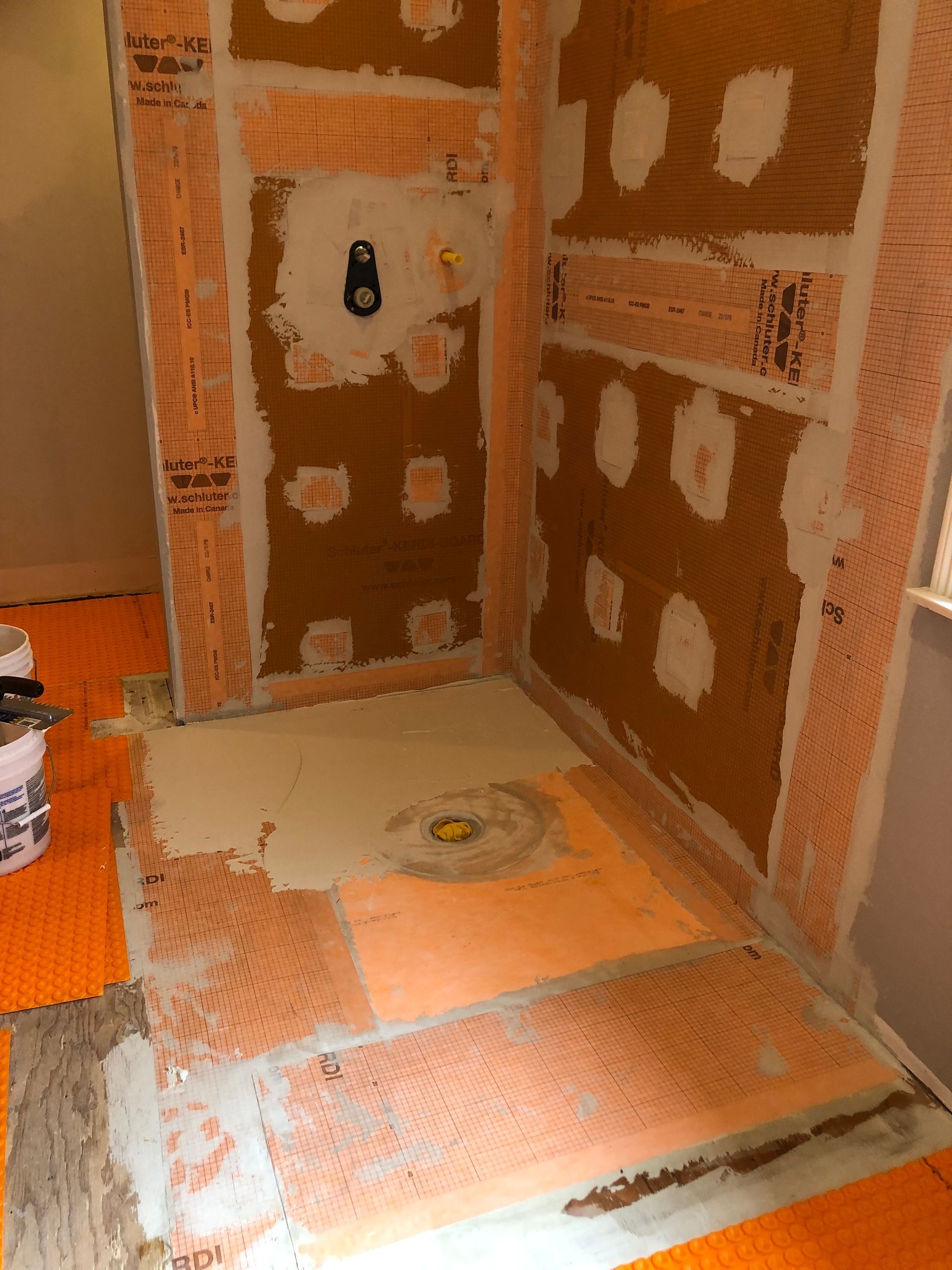 Bathroom shower under construction with orange waterproof membrane.