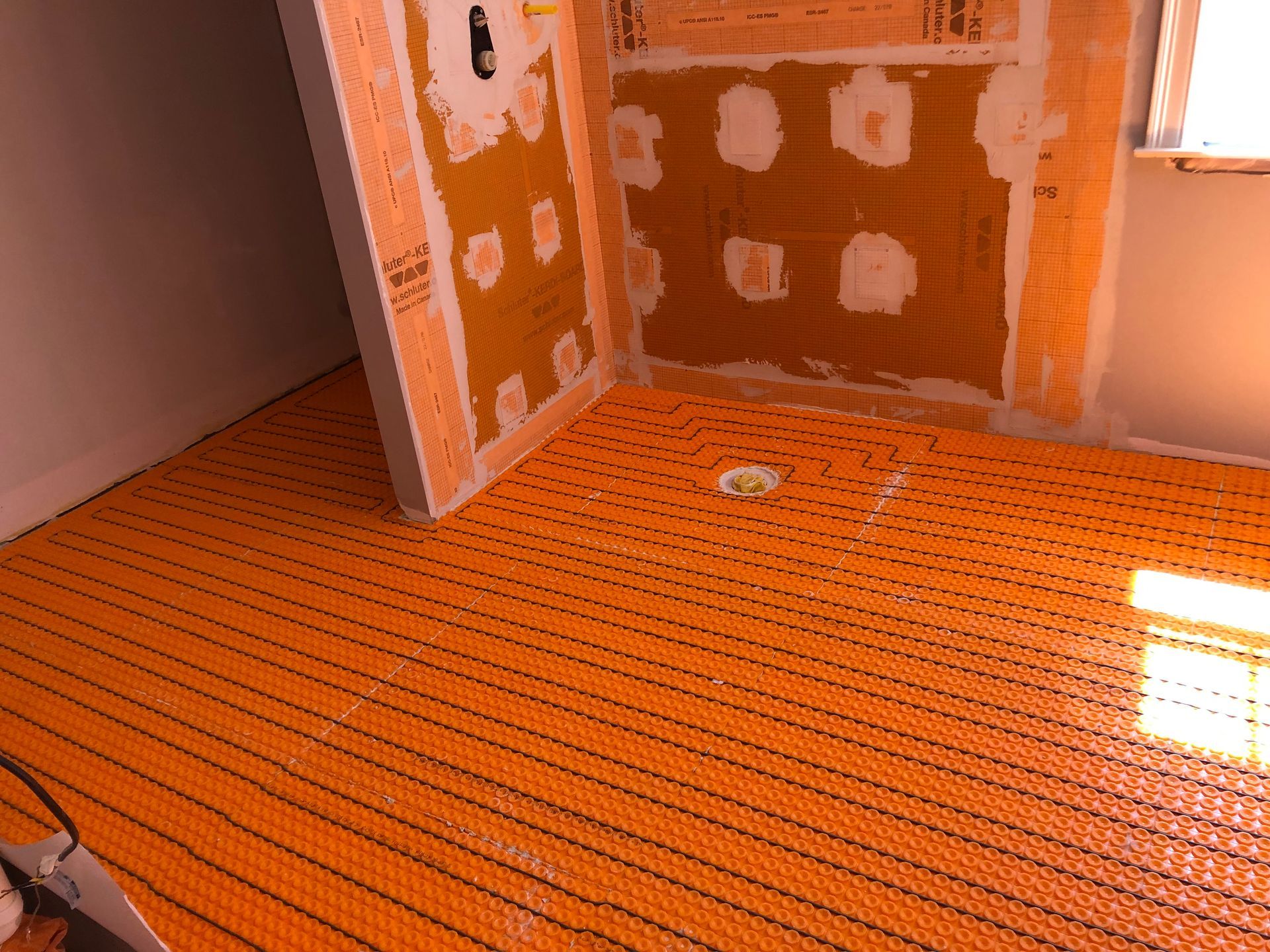 Orange floor heating mat installed in a bathroom, near shower walls.