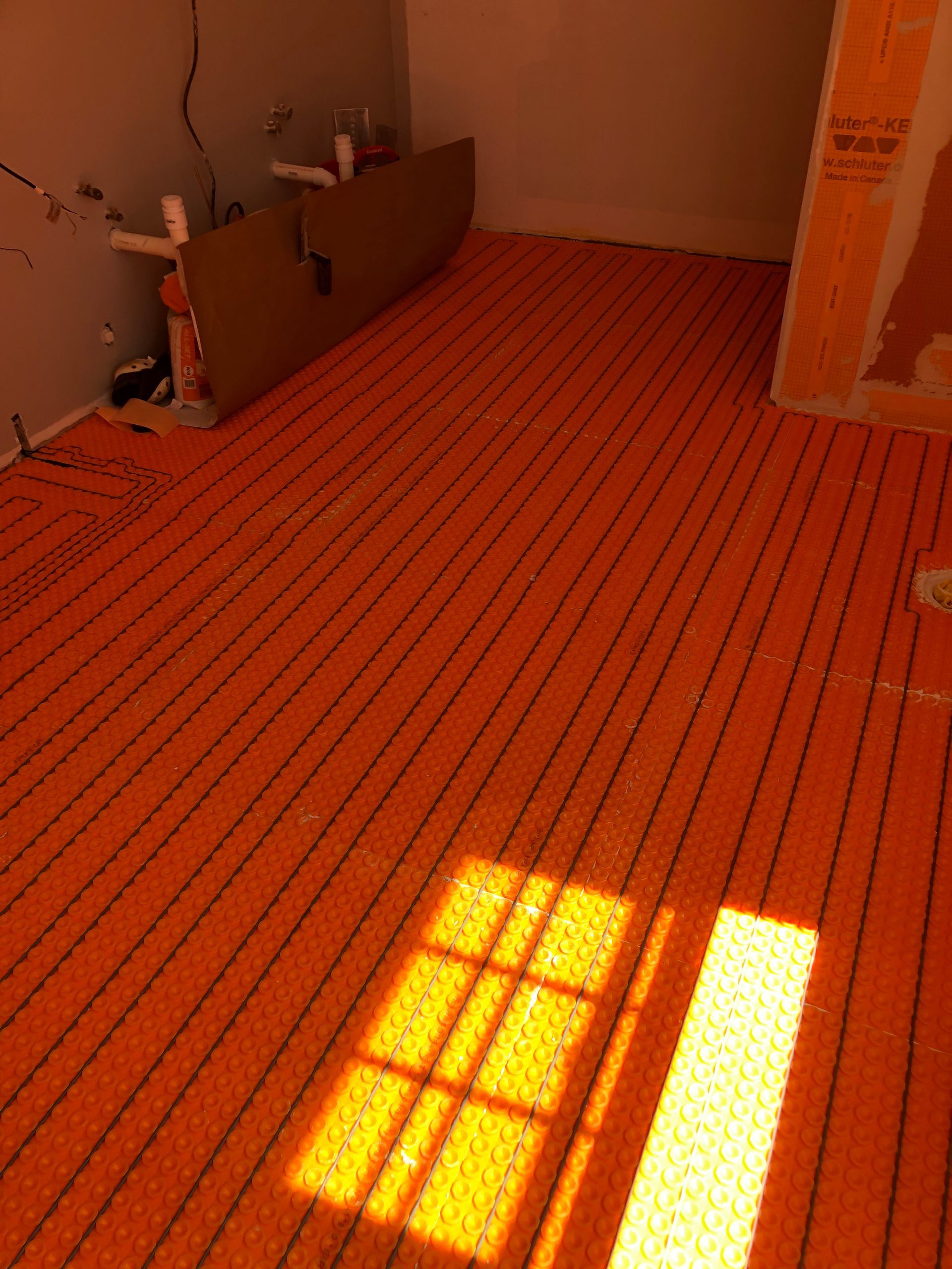 Orange radiant floor heating mat installed in a bathroom, with sunlight illuminating the floor.