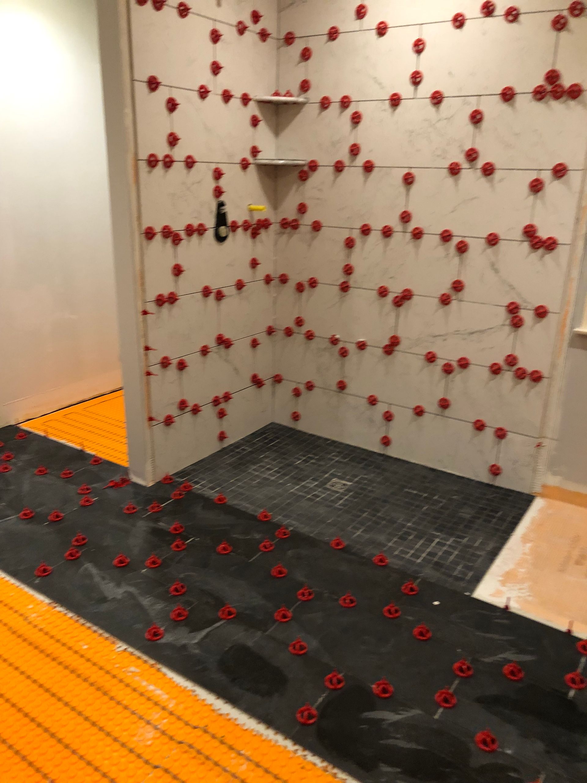 Bathroom under construction, tiled walls and floor with leveling system. Orange heating element in floor.