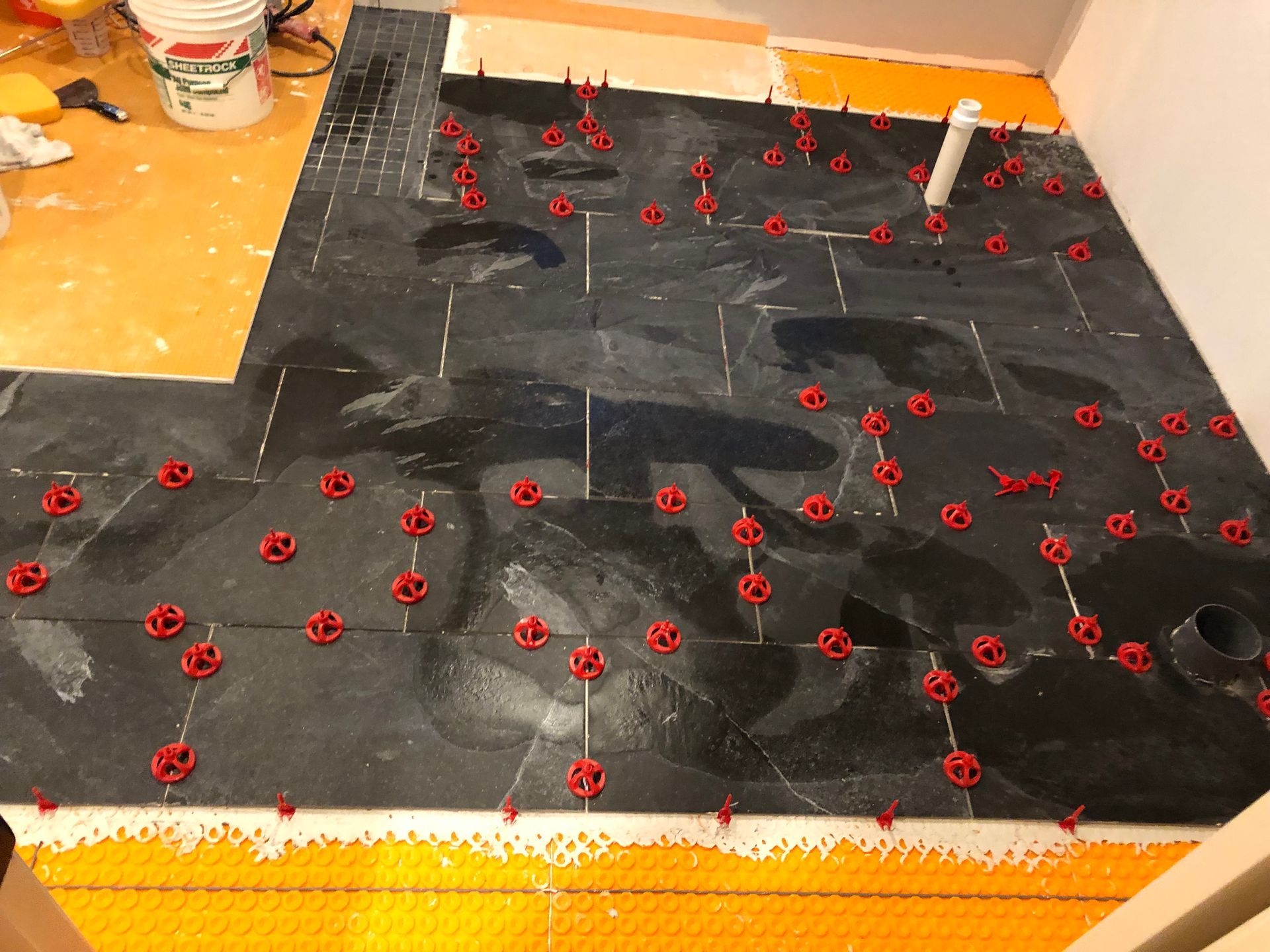 Black tiles being installed on an orange floor, with red leveling system clips.