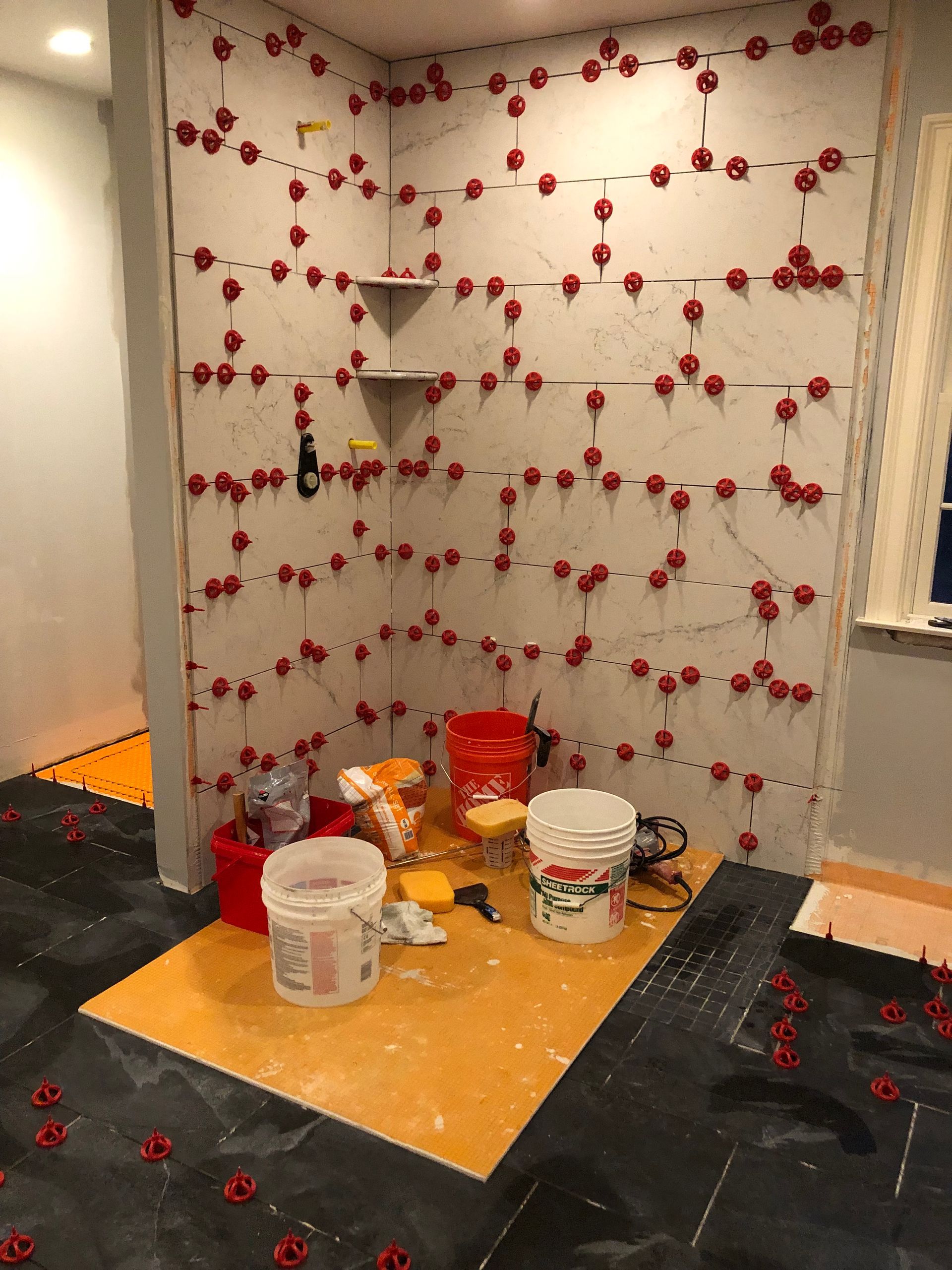 Shower tiling in progress with red leveling spacers; tools and materials are on the floor.