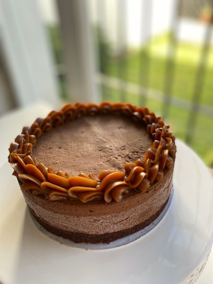 Tarta de queso de chocolate con glaseado de caramelo en un plato blanco; luz natural de fondo.
