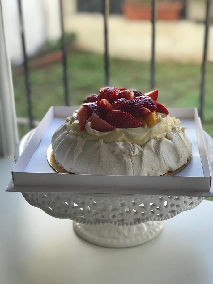 Pastel Pavlova con fresas sobre un soporte para tartas blanco, frente a una ventana.