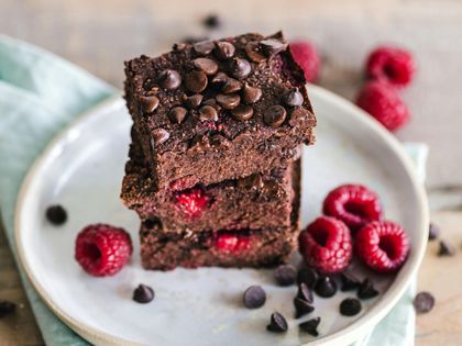 Pila de brownies de chocolate con chispas de chocolate y frambuesas en un plato.