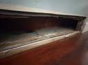 Open wooden vent in a wall, showing the interior. Dark, dusty, with wooden floor in front.