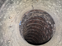 Looking down a dark, dirty, flexible duct, round with ridged, gray interior walls.