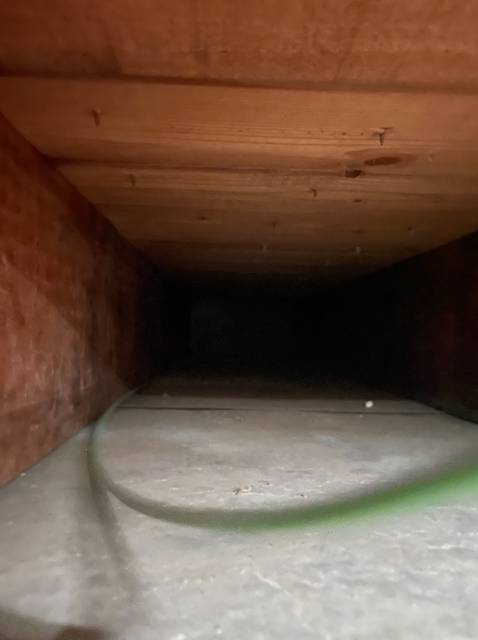 Inside a dark rectangular duct with wooden sides and a concrete floor; green wire visible.