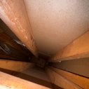 View inside an attic with wooden beams and insulation on the ceiling.