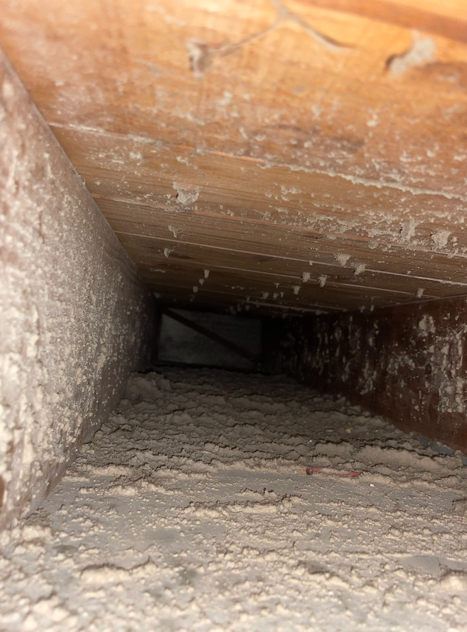 Dust-covered wooden air duct. Interior view looking down a narrow, rectangular passage.