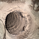 A dusty, circular vent opening inside a wall, with a layered, textured surface.