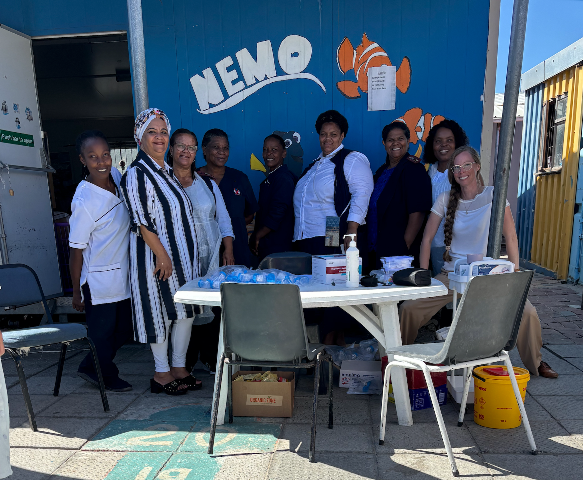 Group of people standing behind a table at an outdoor NEMO booth with a blue wall and signage.