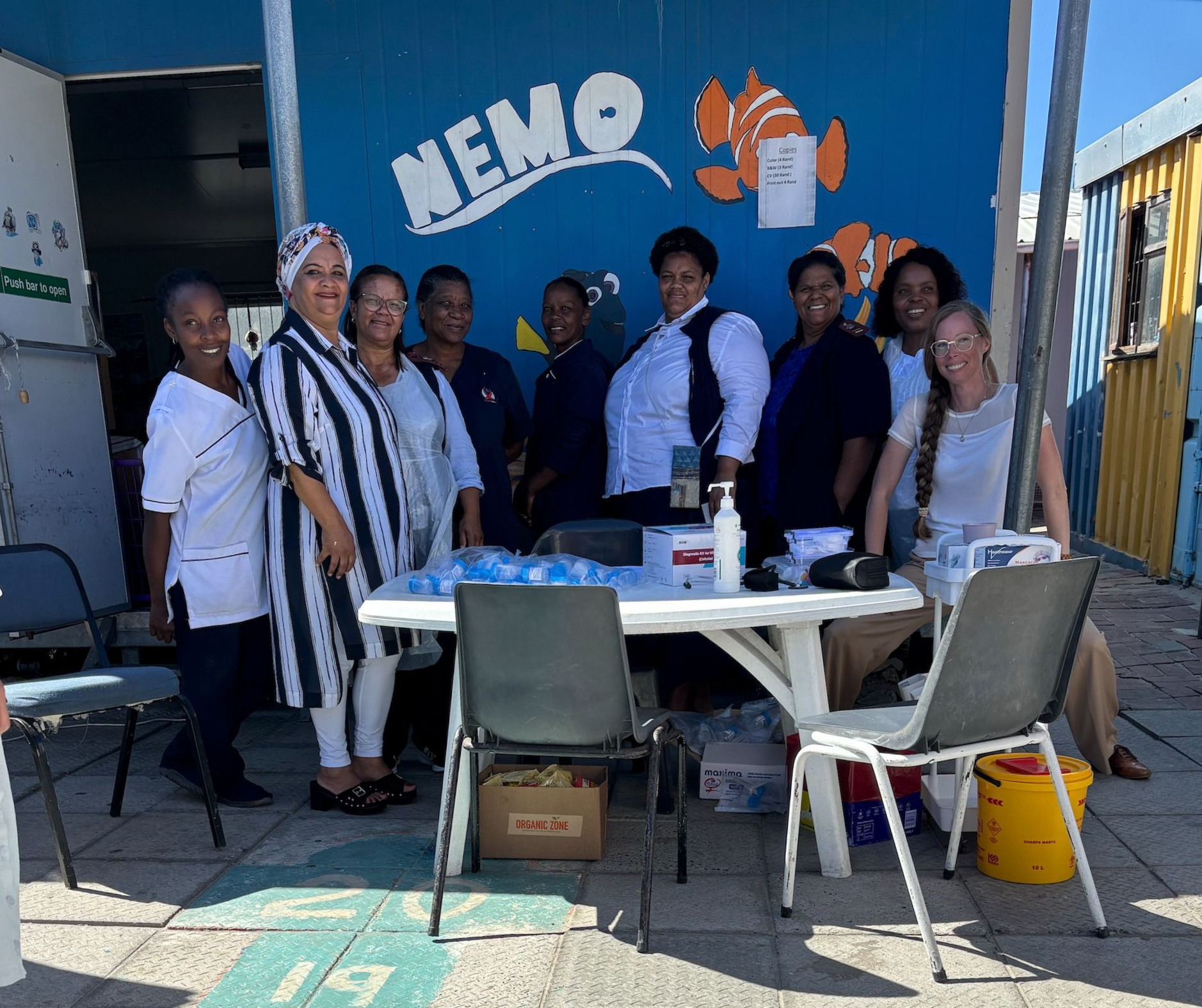 Group of people standing behind a table at an outdoor NEMO booth with a blue wall and signage.