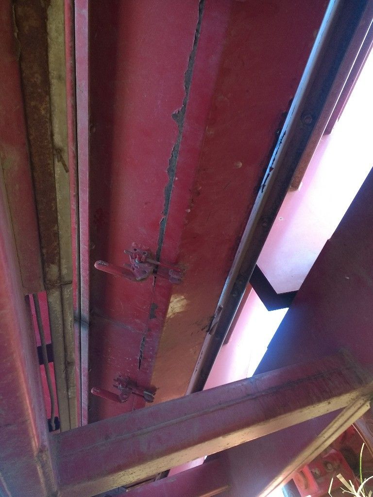 Viga de acero roja con óxido y una grieta, sostenida por vigas de madera.