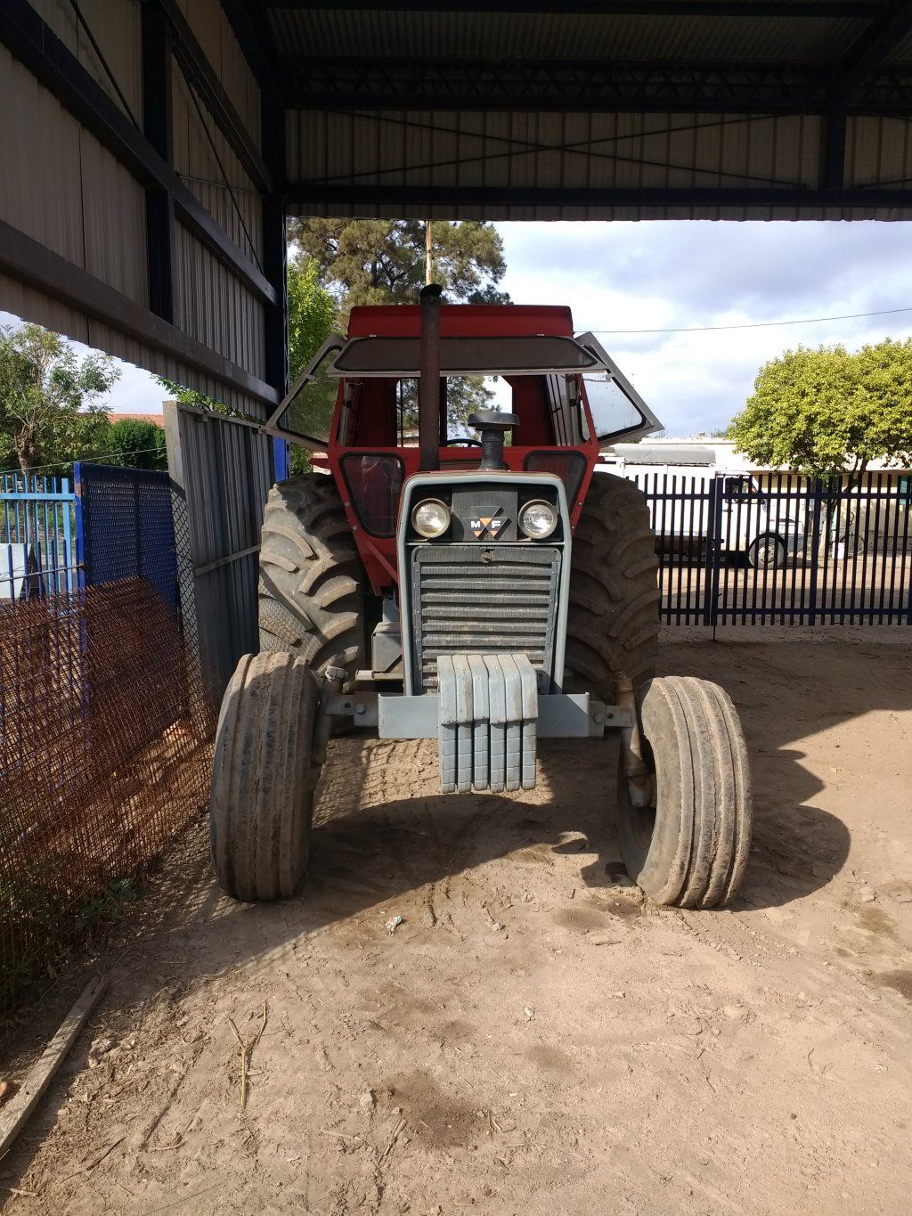 Tractor Massey Ferguson rojo y gris con neumáticos grandes, debajo de un cobertizo.