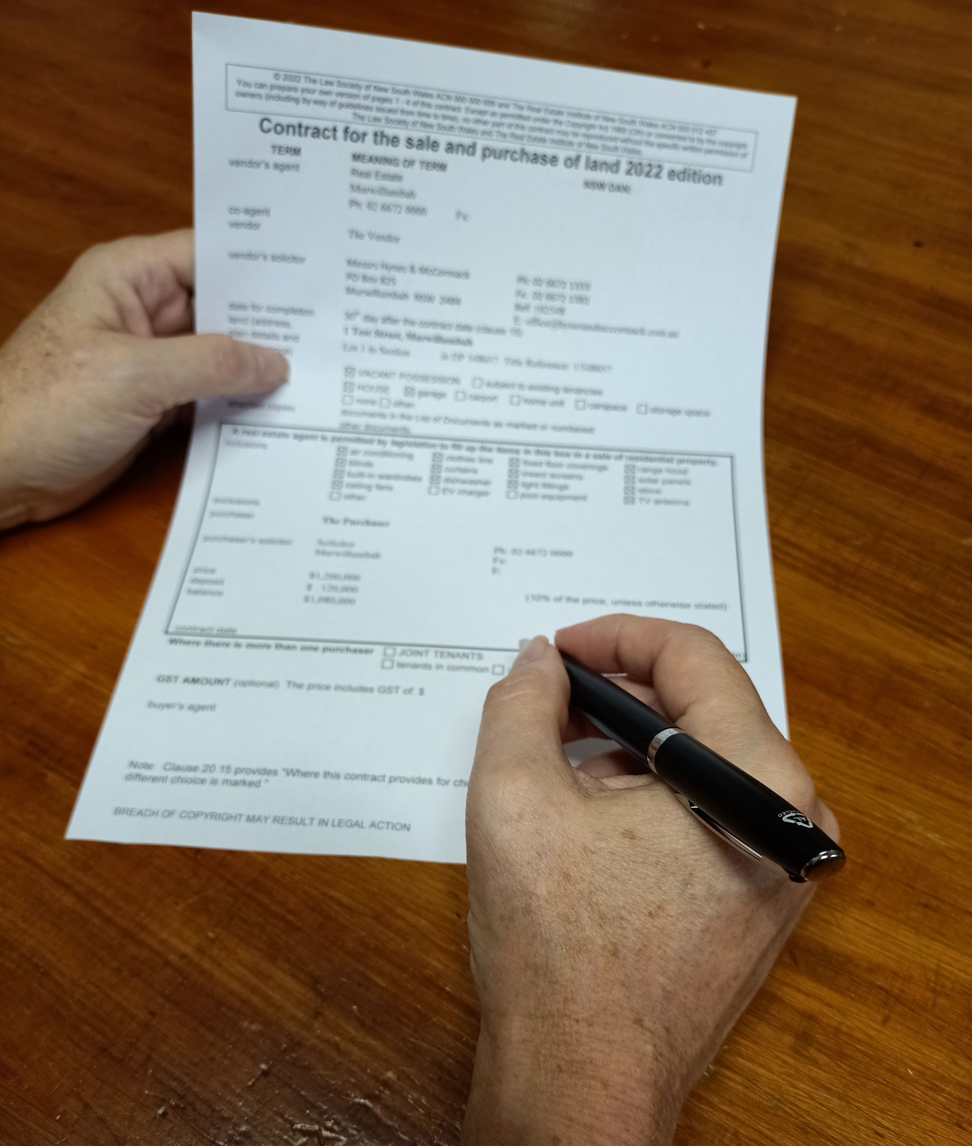 A Man is Pointing at a Person Signing a Contract — Hynes & McCormack In Murwillumbah, NSW