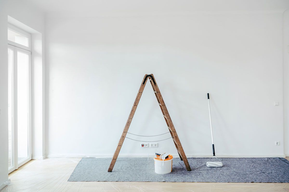 An empty room with a ladder , mop , and paint bucket.