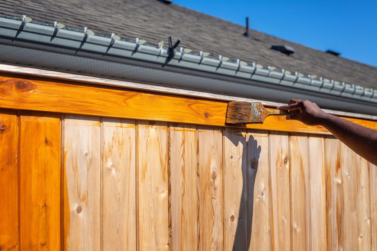A person is painting a wooden fence with a brush.