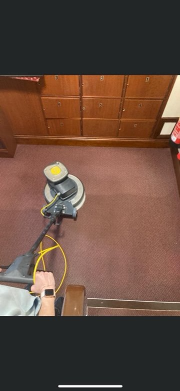 A person is cleaning a carpet with a machine in a room.