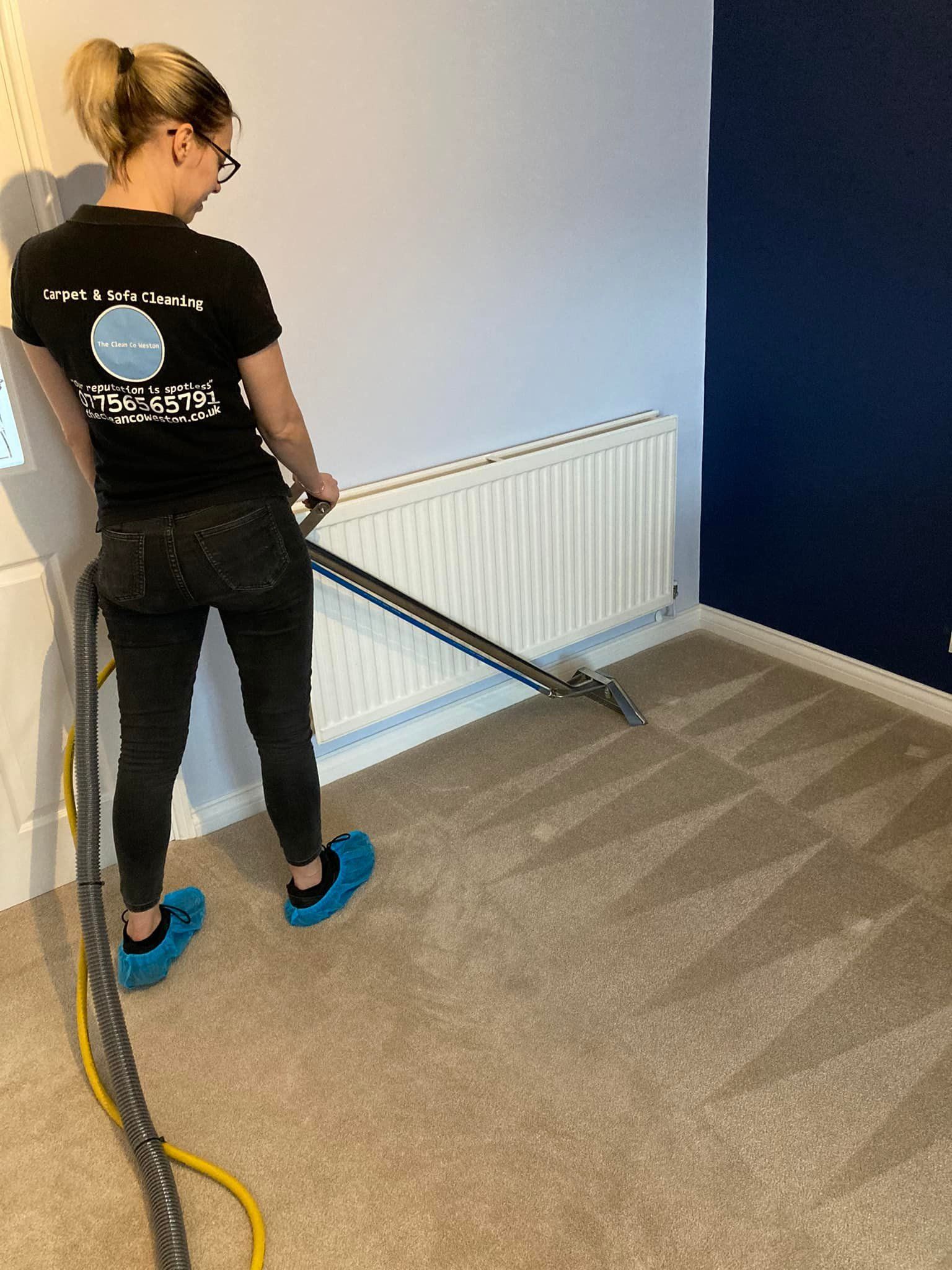 A woman is cleaning a carpet with a vacuum cleaner.