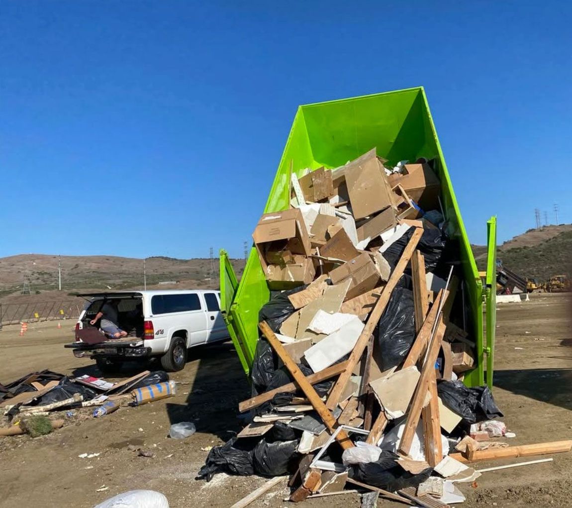 A green dumpster filled with lots of trash and boxes