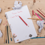 A notebook with a pencil on it is sitting on a wooden table.