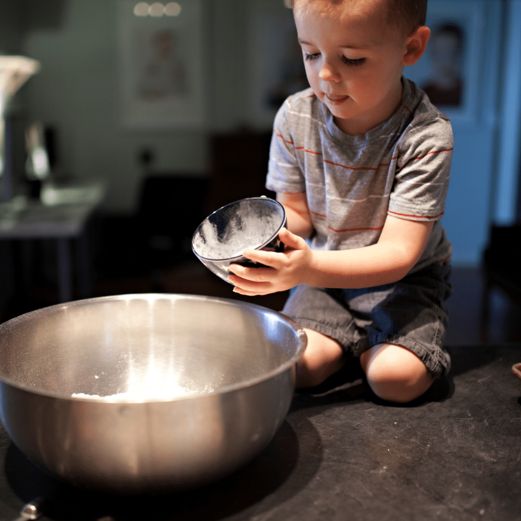A little boy is sitting on a counter holding a bowl of flour