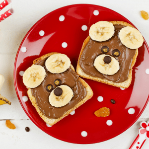 Two slices of teddy bear toast with chocolate and bananas on a red plate