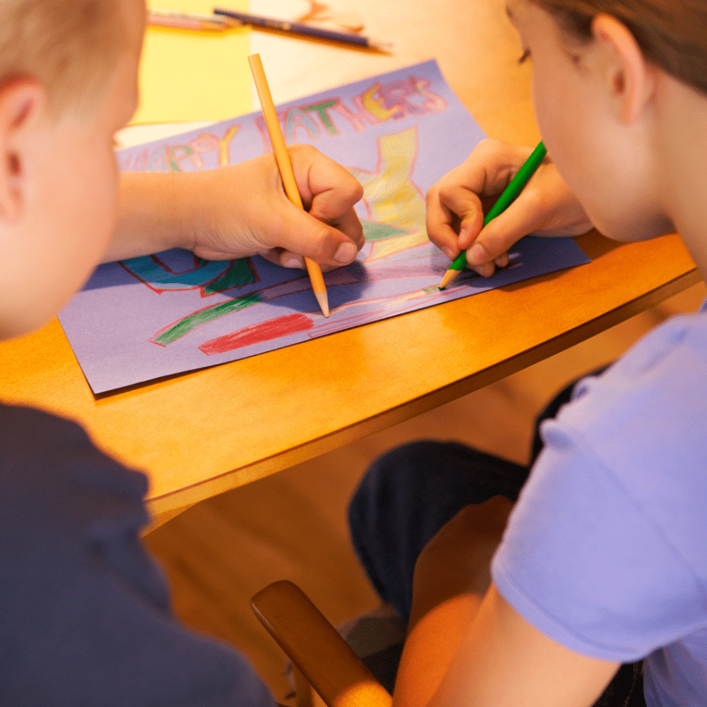 A boy and a girl are sitting at a table drawing with pencils